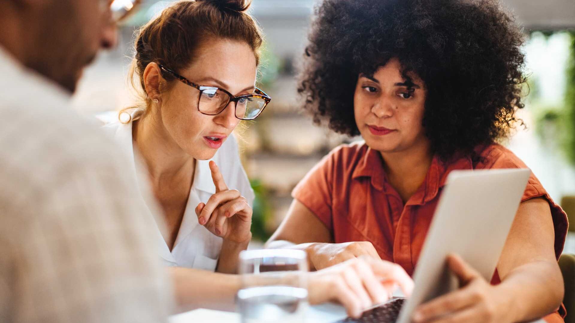 Two female colleagues look at an open laptop in an office setting