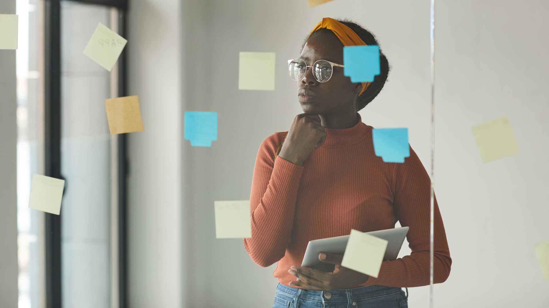 Leader/worker standing at a glass board with sticky notes, pensively.