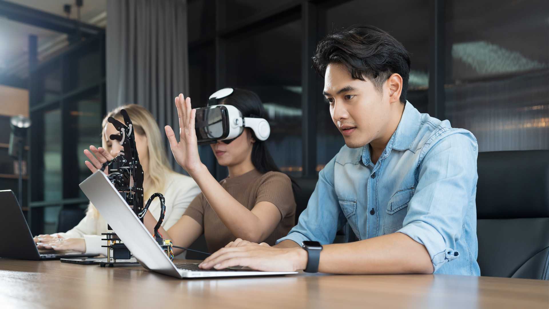 people sitting at a desk working with vr glasses to control robot arm system