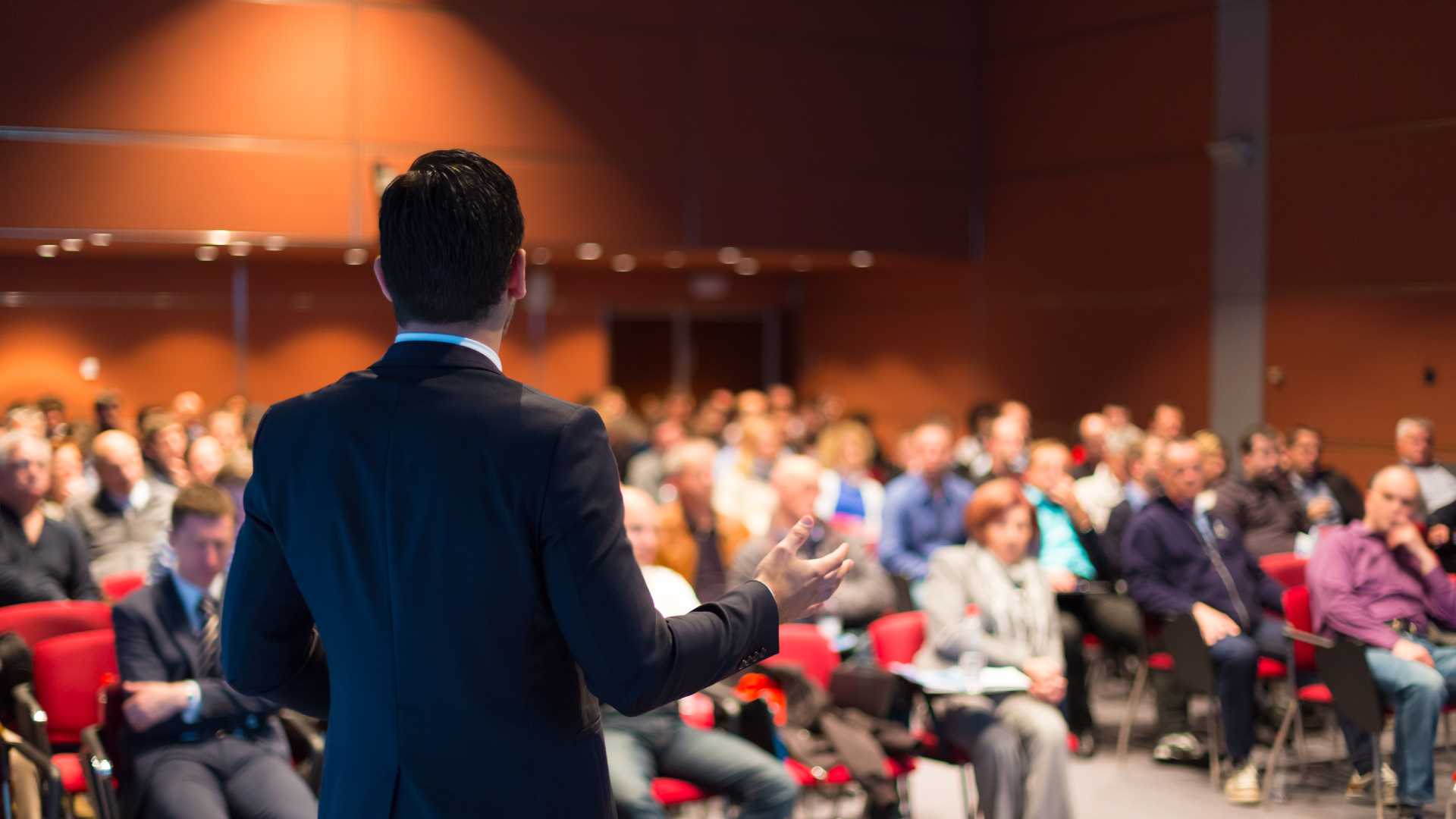 Speaker in a suit addressing an auditorium of people.