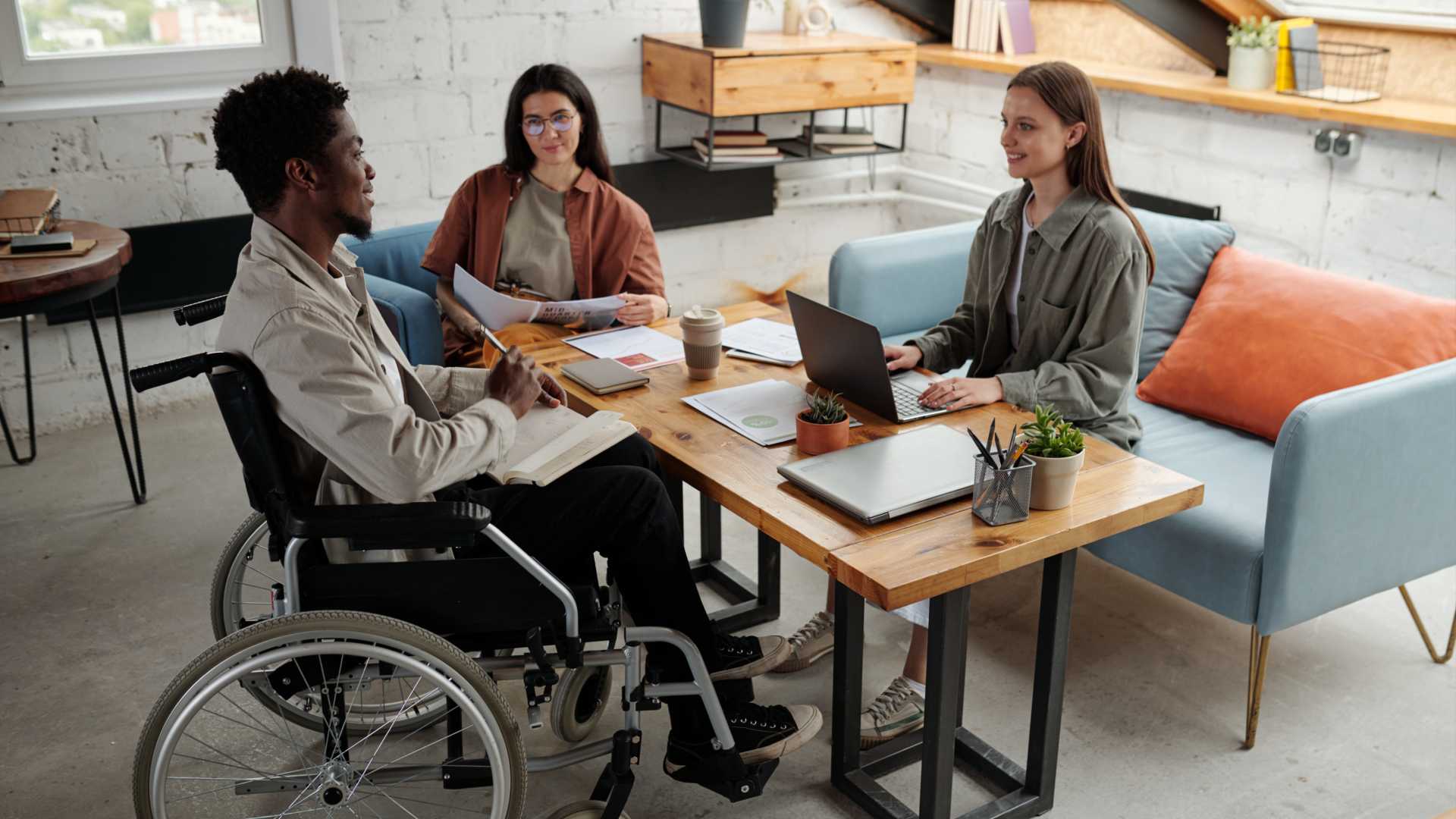 A diverse group of coworkers meets in a casual setting. One of the coworkers is using a wheelchair.