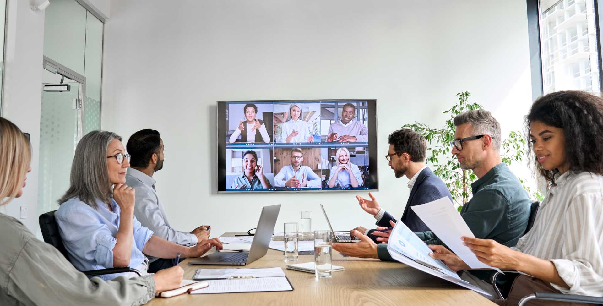A hybrid team meeting with virtual participants joining showcased on a TV mounted on a wall