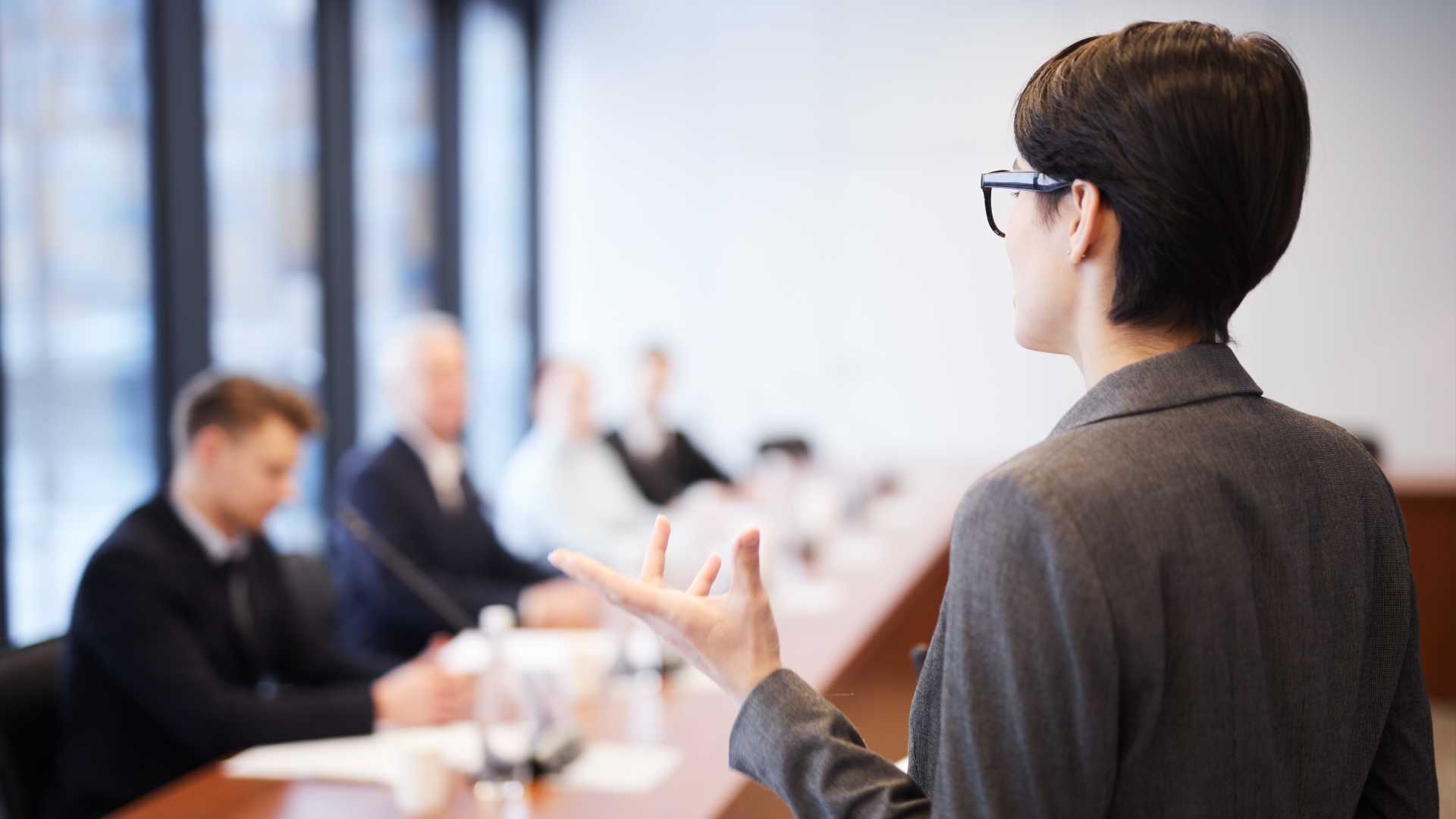 A businessperson gives a presentation in front of an executive boardroom