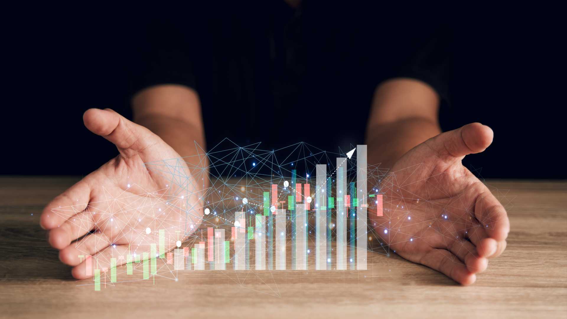 Two hands spread open on a wood desk; a holographic bar graph in the middle