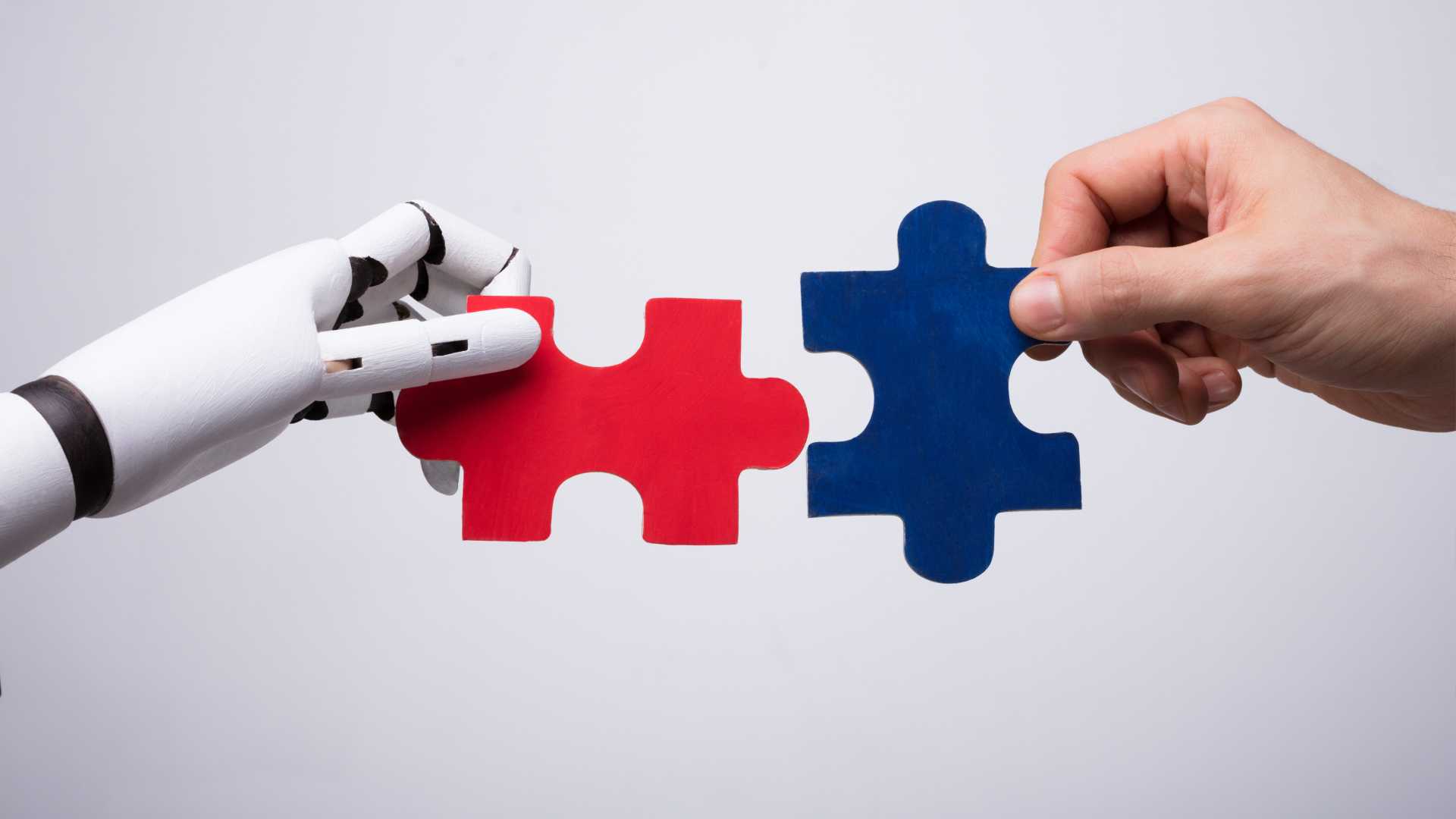 A human hand and a robot hand hold up two puzzle pieces, about to fit them together.