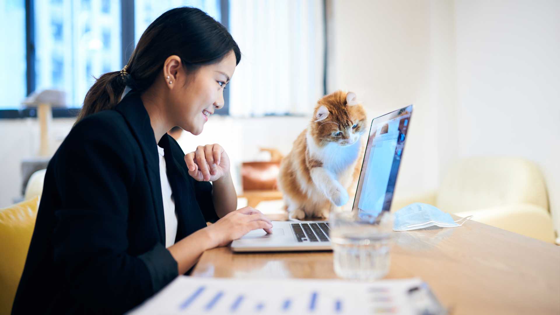 A woman works from home in front of an open laptop next to a cat