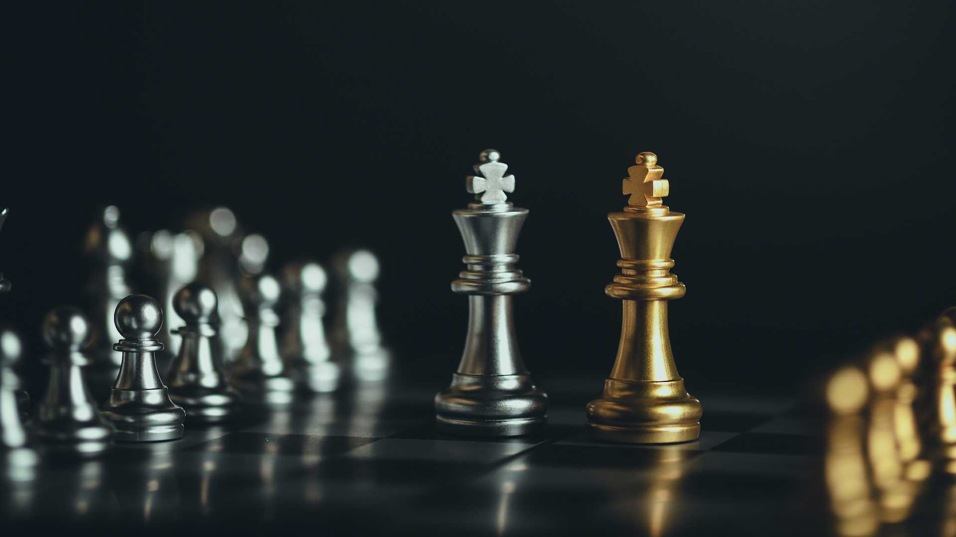 silver and gold chess pieces are lined up on a board with two centered