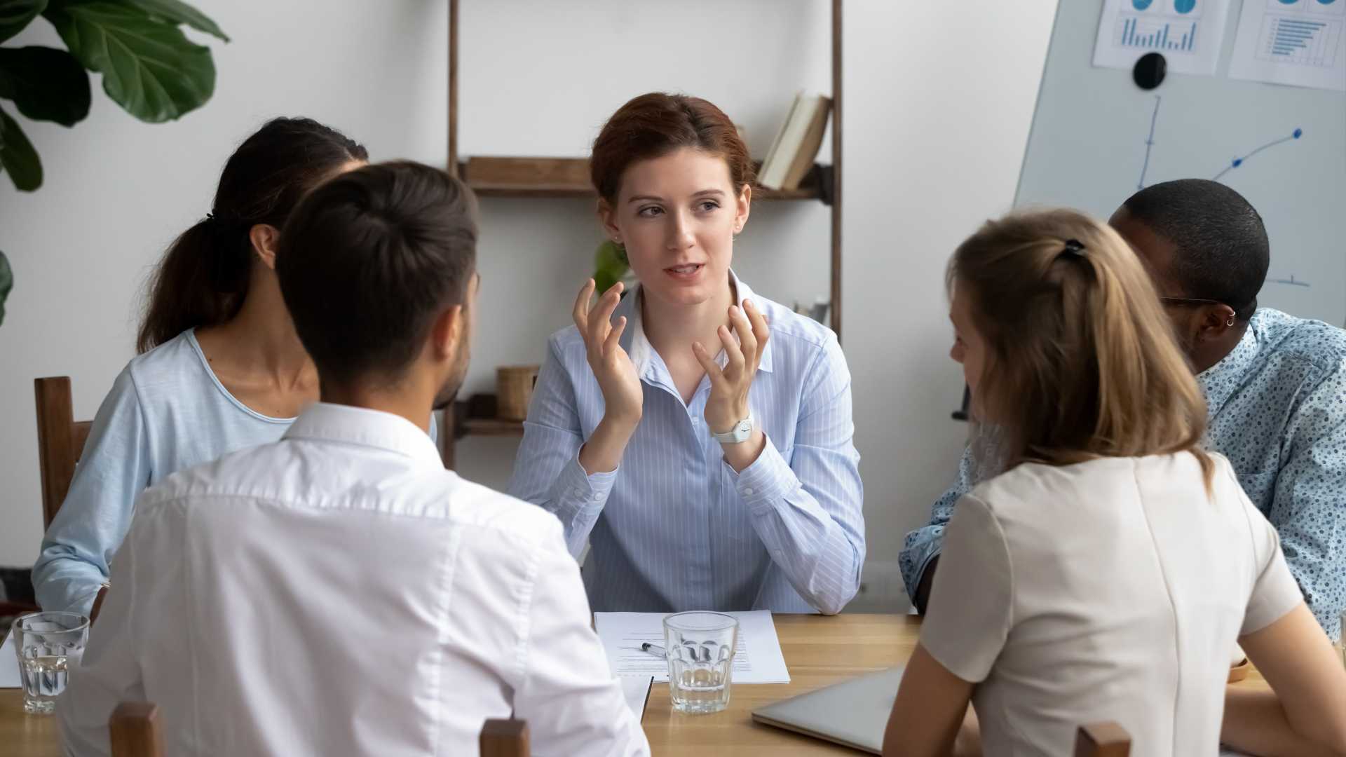Five people brainstorming sitting around desk in briefing at boardroom.