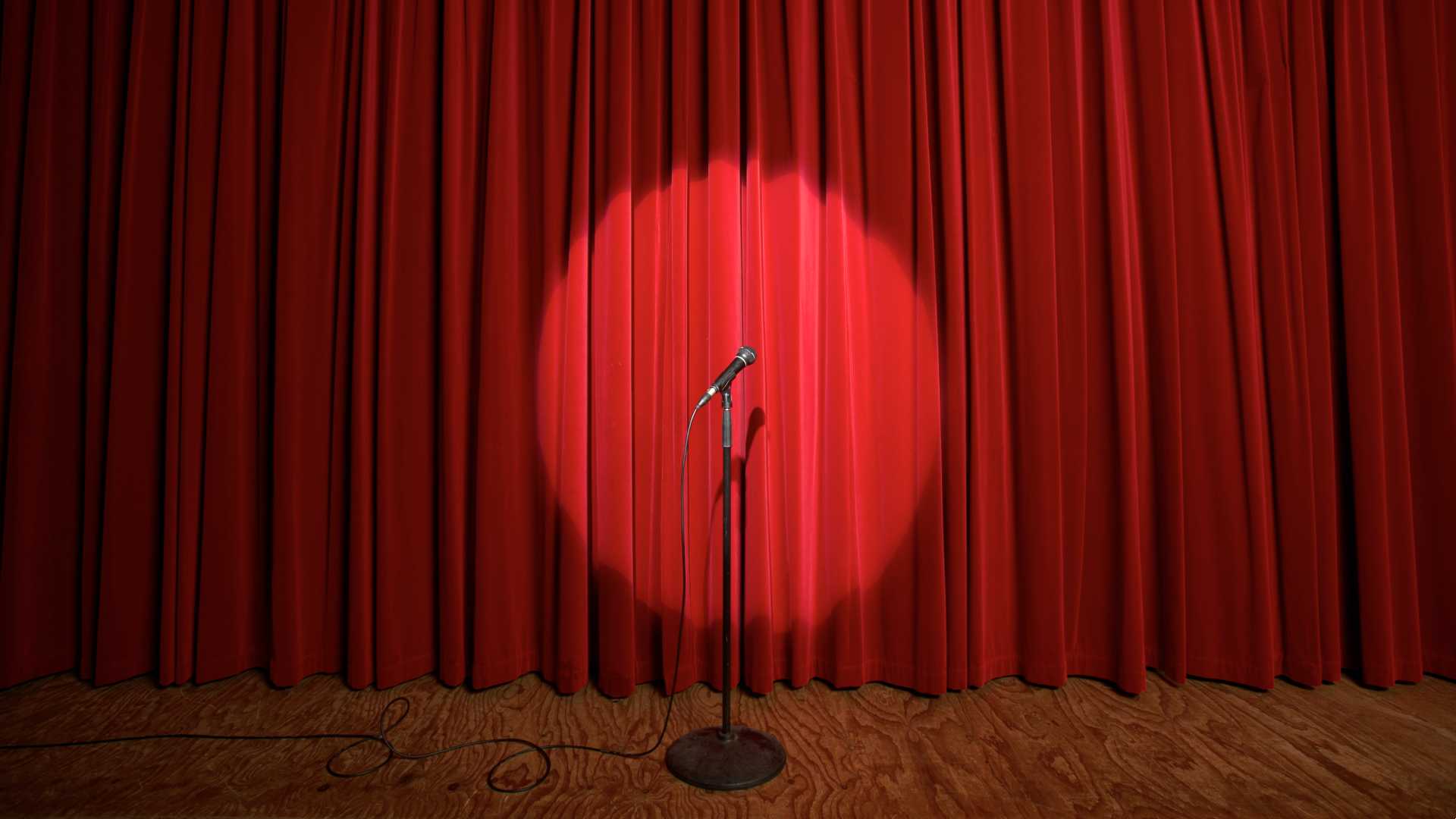 A microphone stands in front of a red curtain, creating an atmosphere of anticipation and performance.