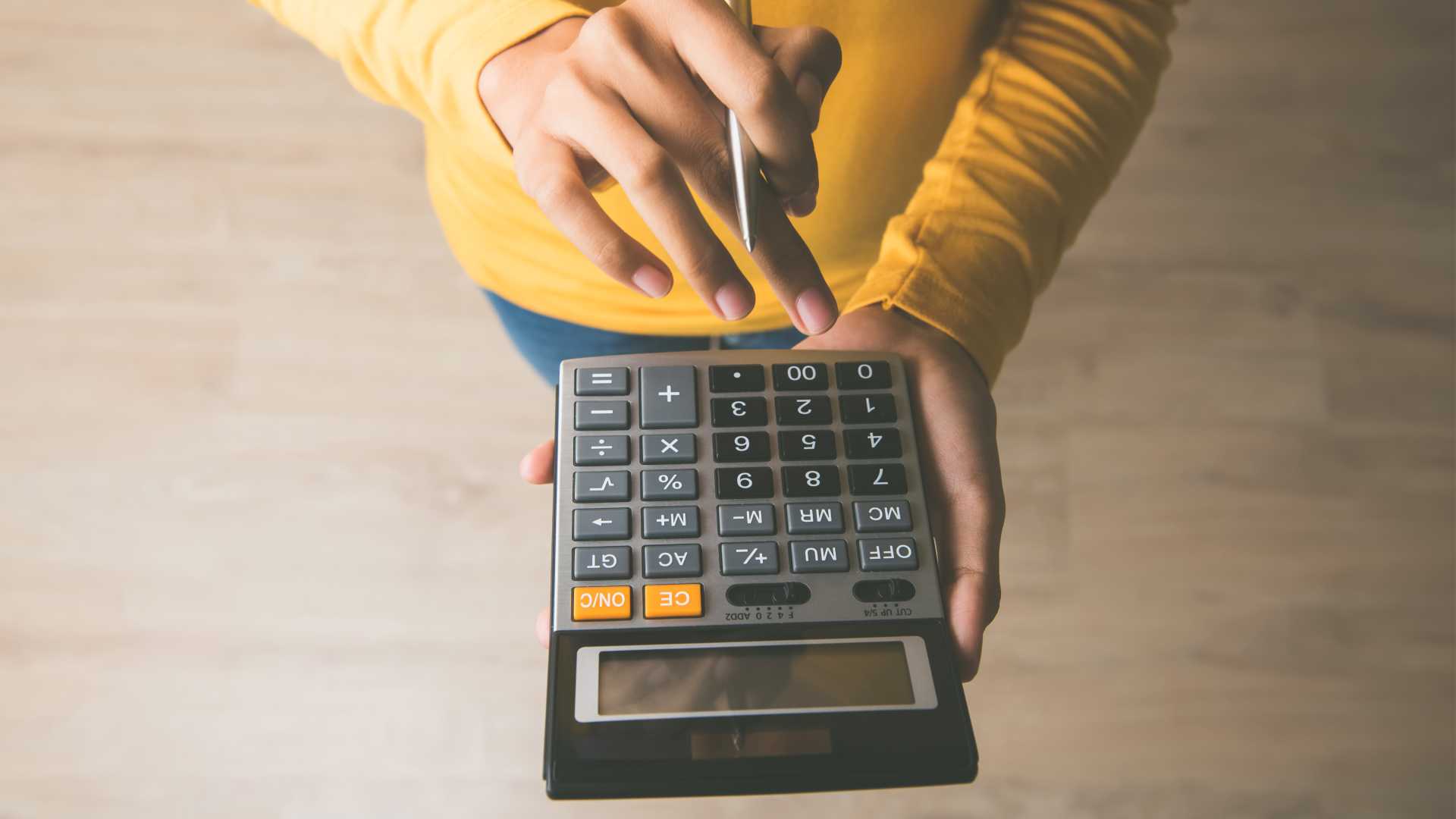Person in a yellow sweater, holding a pen, using a calculator.