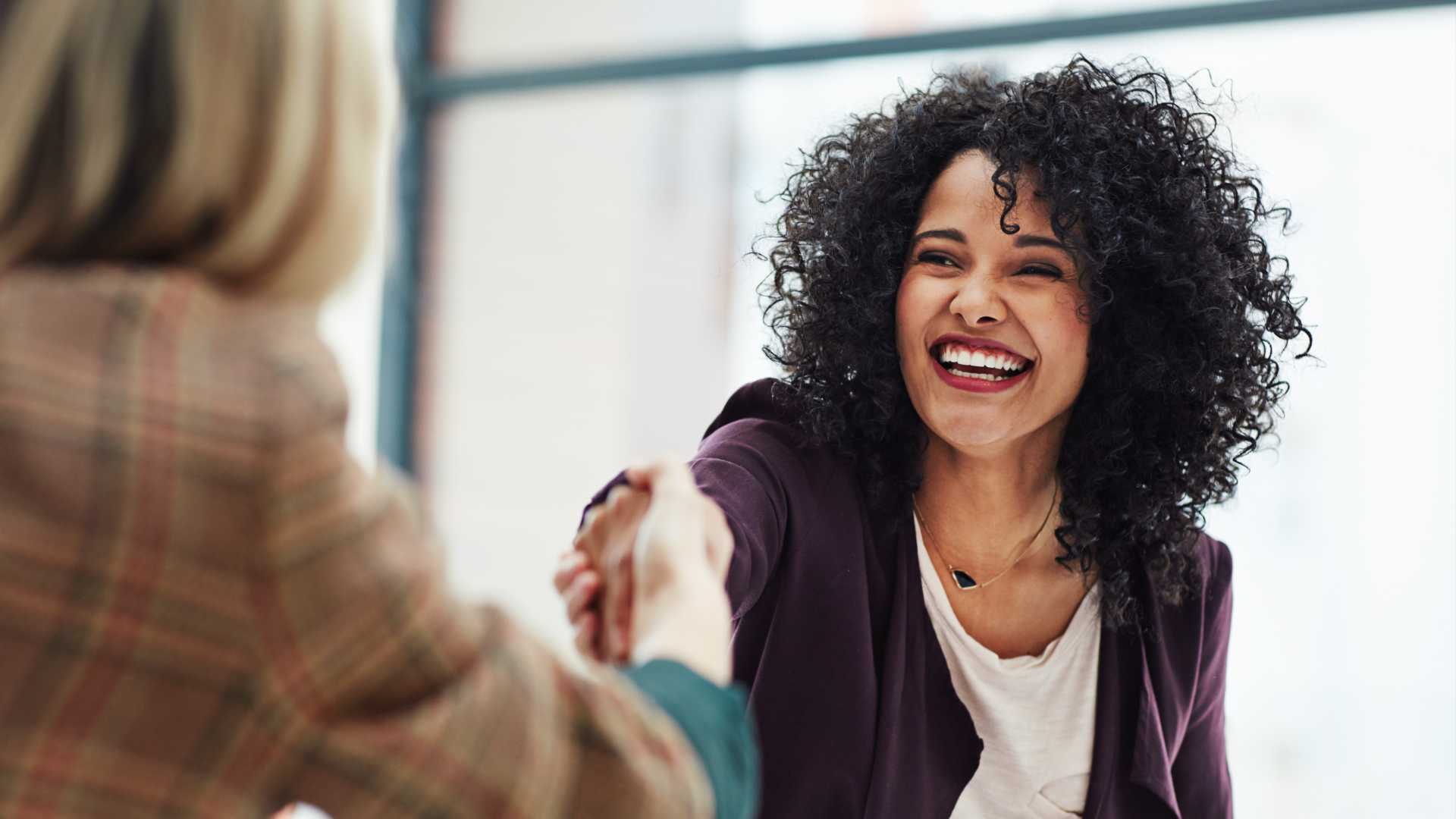 A woman shakes hands with another woman in a professional setting, representing professional networking