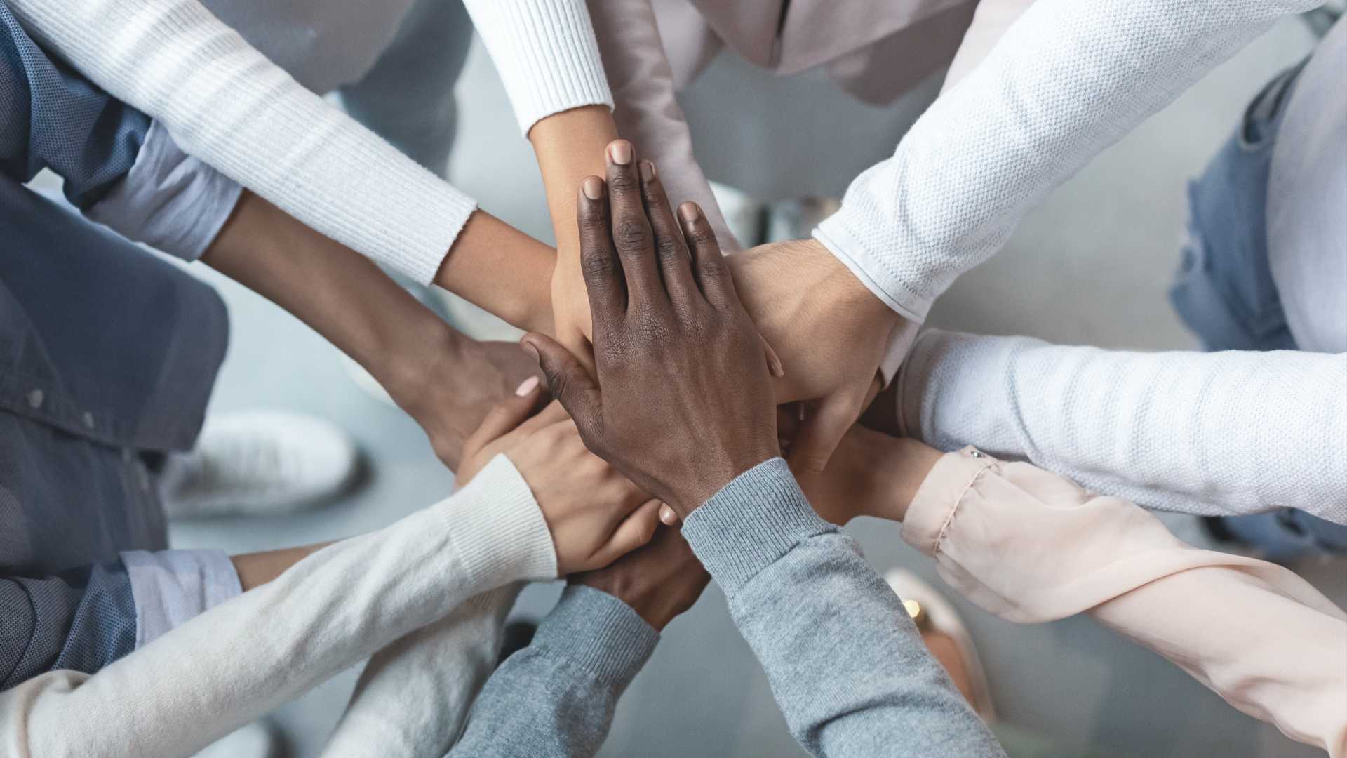 Hands from a group of people on top of each other in the middle like a team.