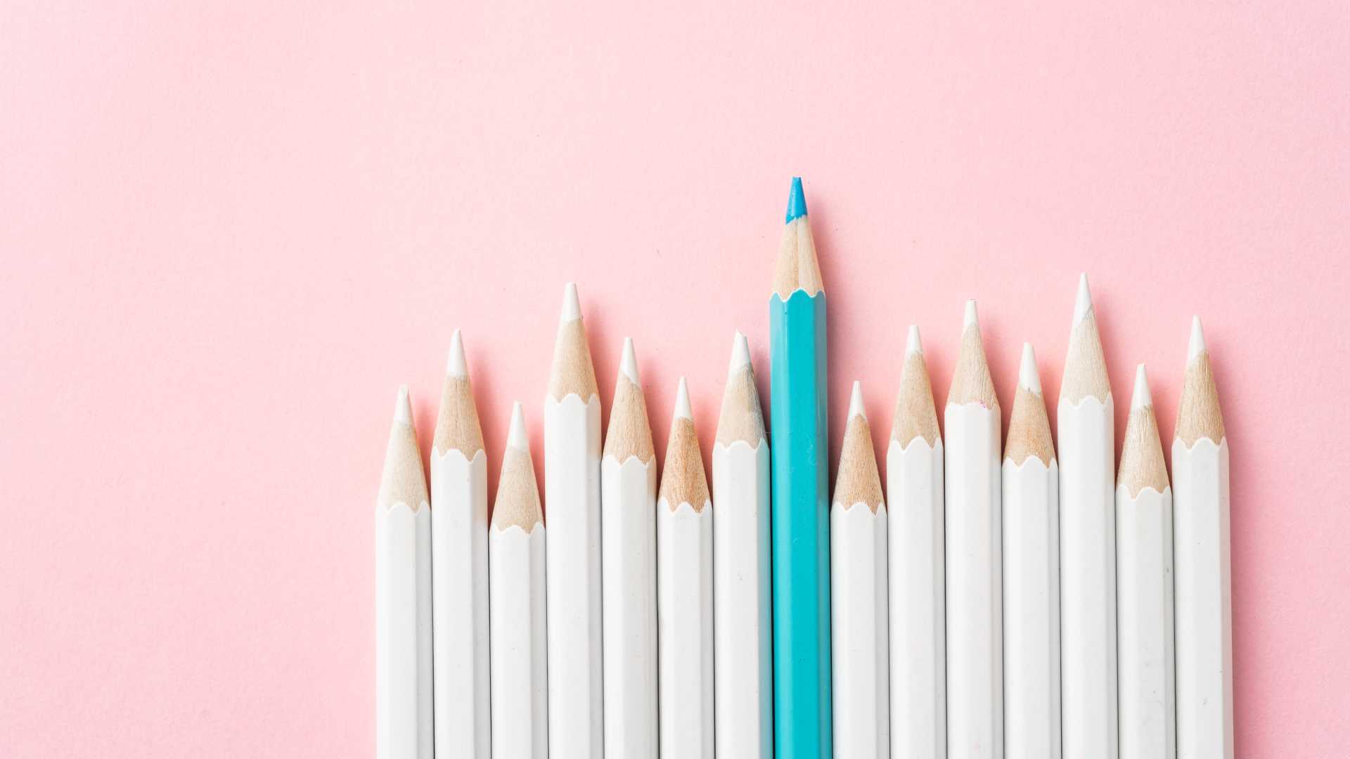 A row of colored pencils are all white except for one blue one that is taller than the others