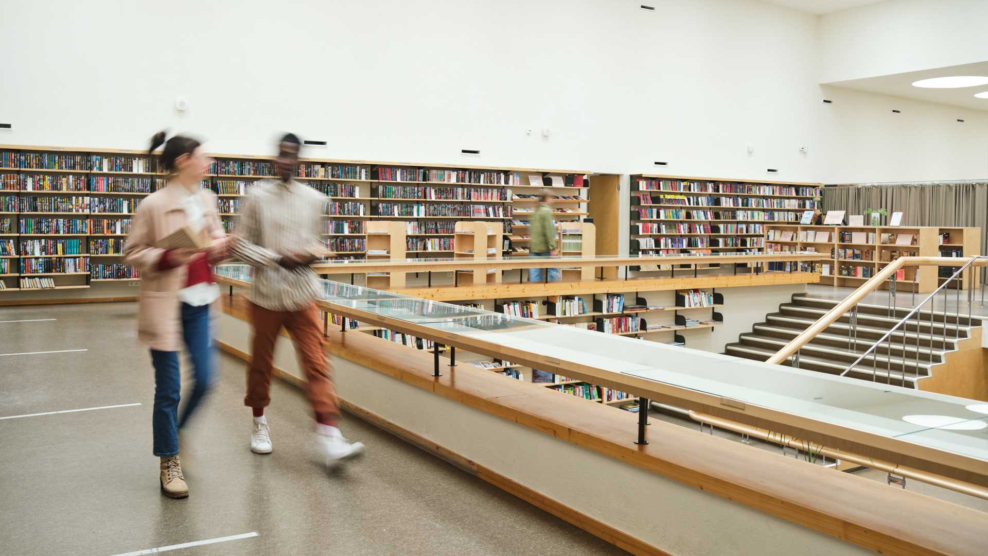 Two university students and/or learners walking through the college library.