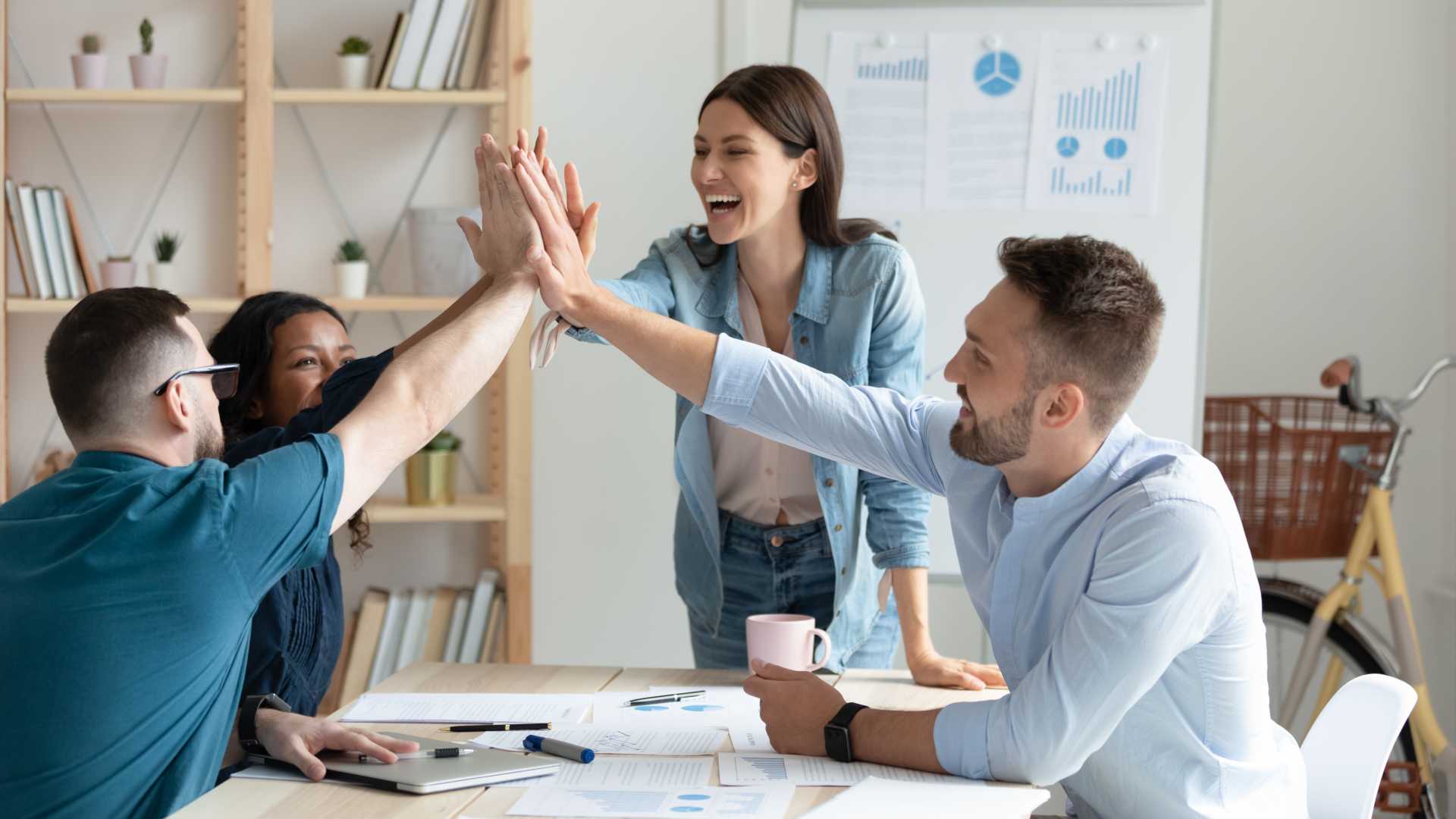a group of people in an office are high fiving with charts and graphs behind them