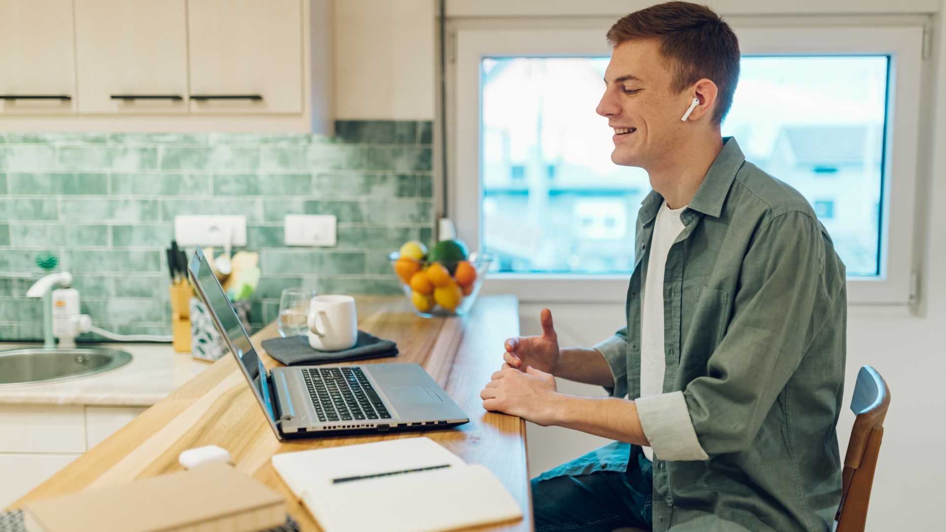 man working on laptop and having a video call in modern kitchen at home.