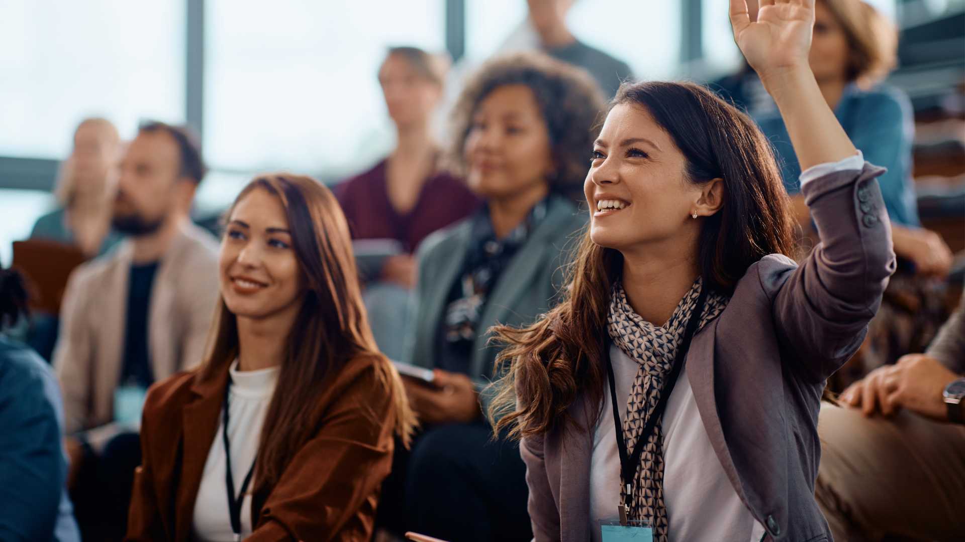 Happy businesswoman raising hand to ask a question attending a seminar in conference hall.