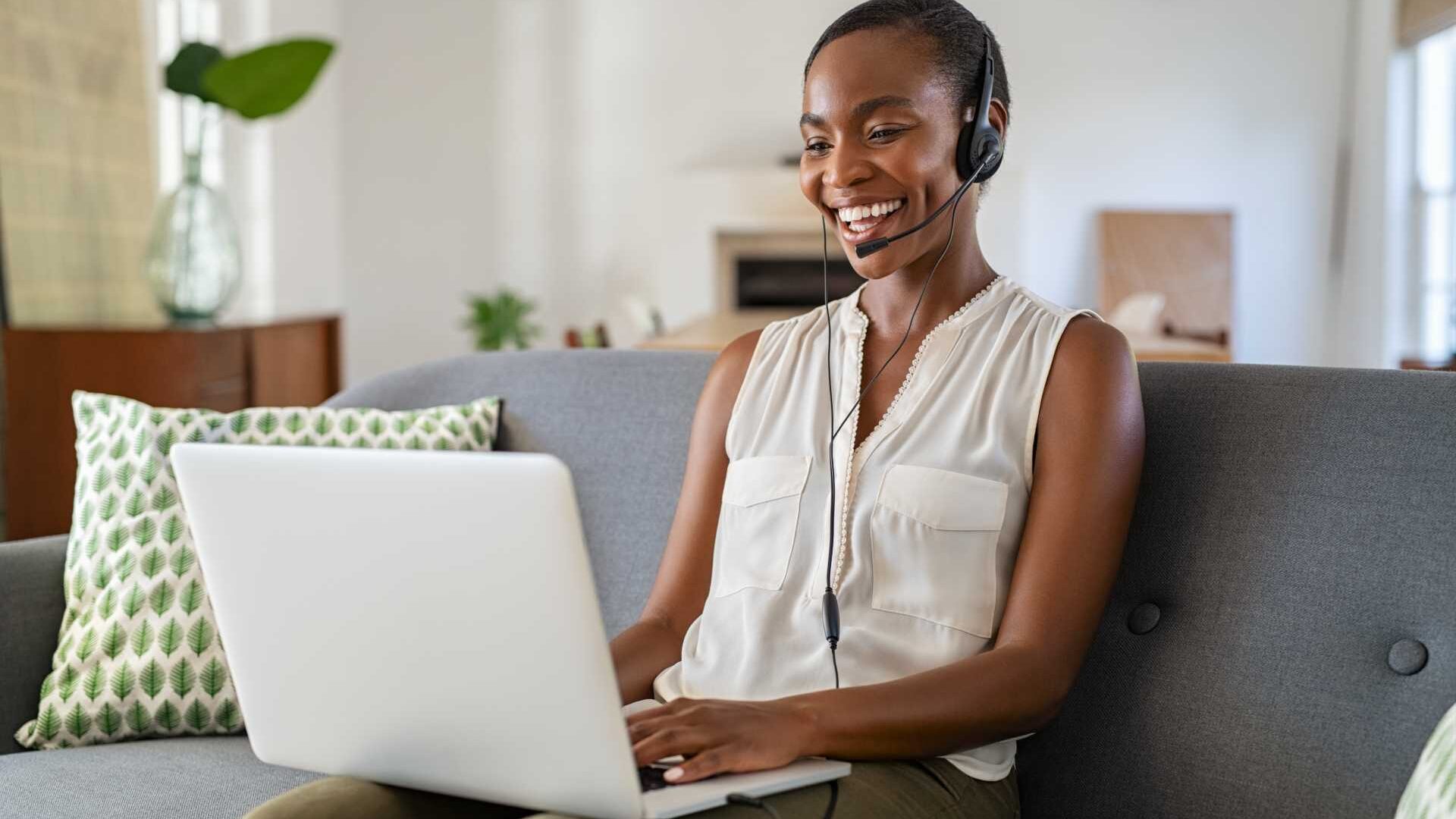 A woman signs on to a virtual meeting from her living room couch