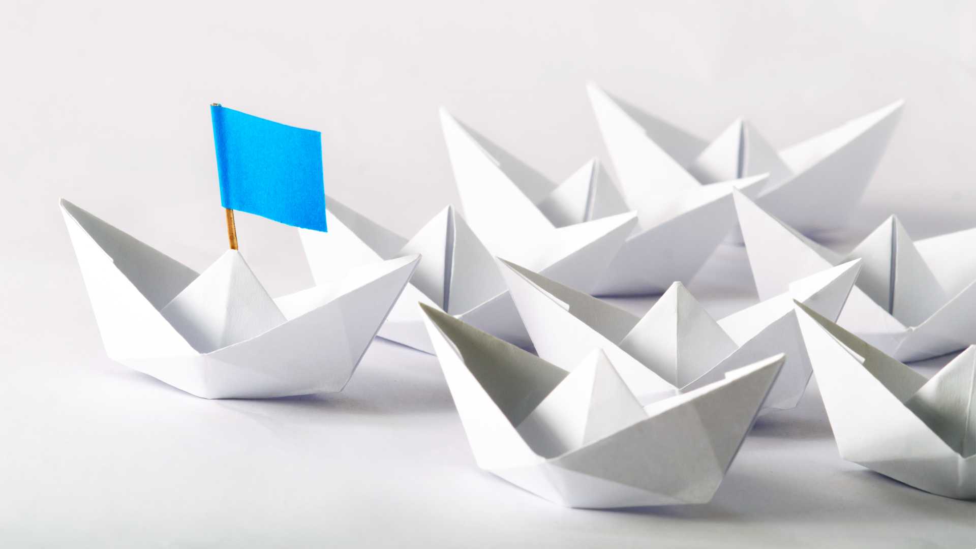 Mini white paper hats following another small paper hat with a blue sail sticking out like a boat.