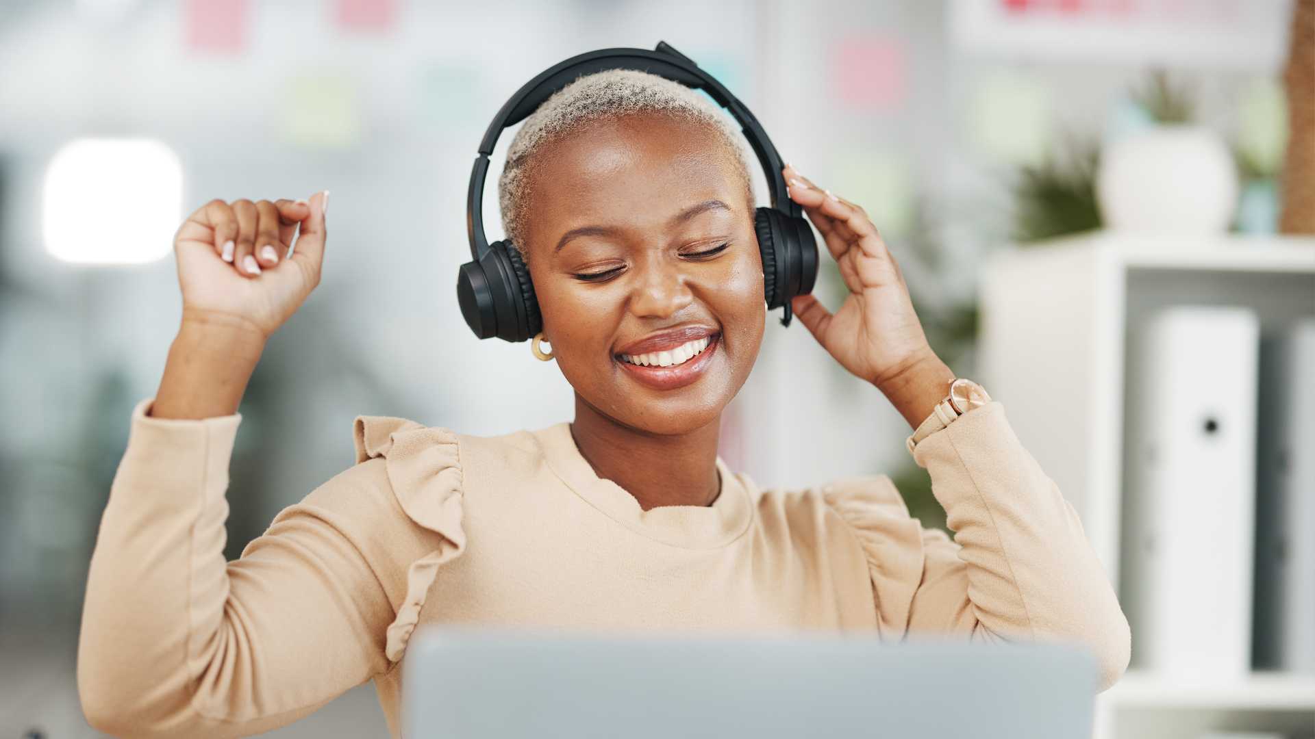 New hire sales rep participating in sales onboarding cheering at their desk with headphone set looking at laptop screen interacting with a possible buyer customer.