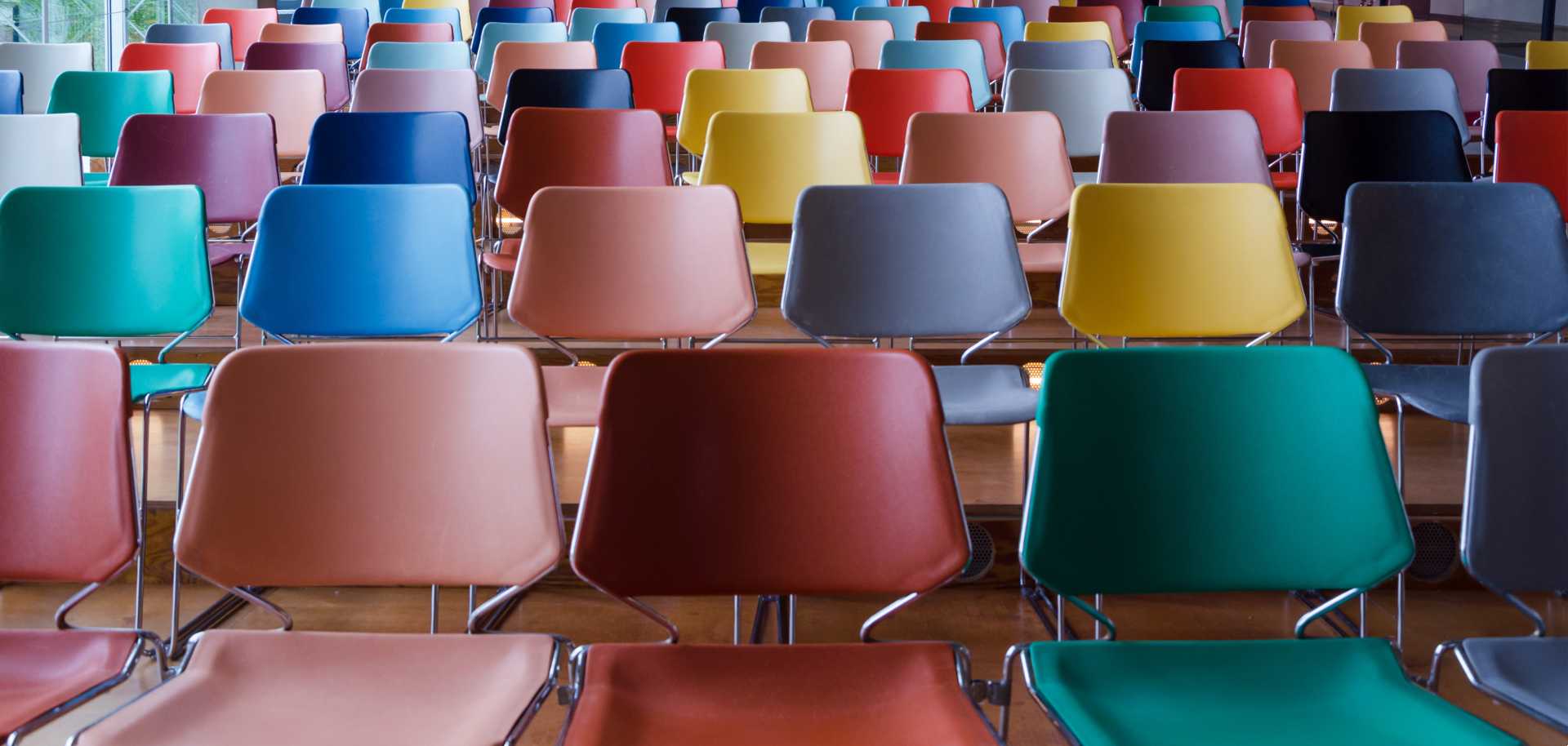 Close up of an auditorium traditional training classroom instructor led training filled with empty multi-hued chairs due to learner disengagement.