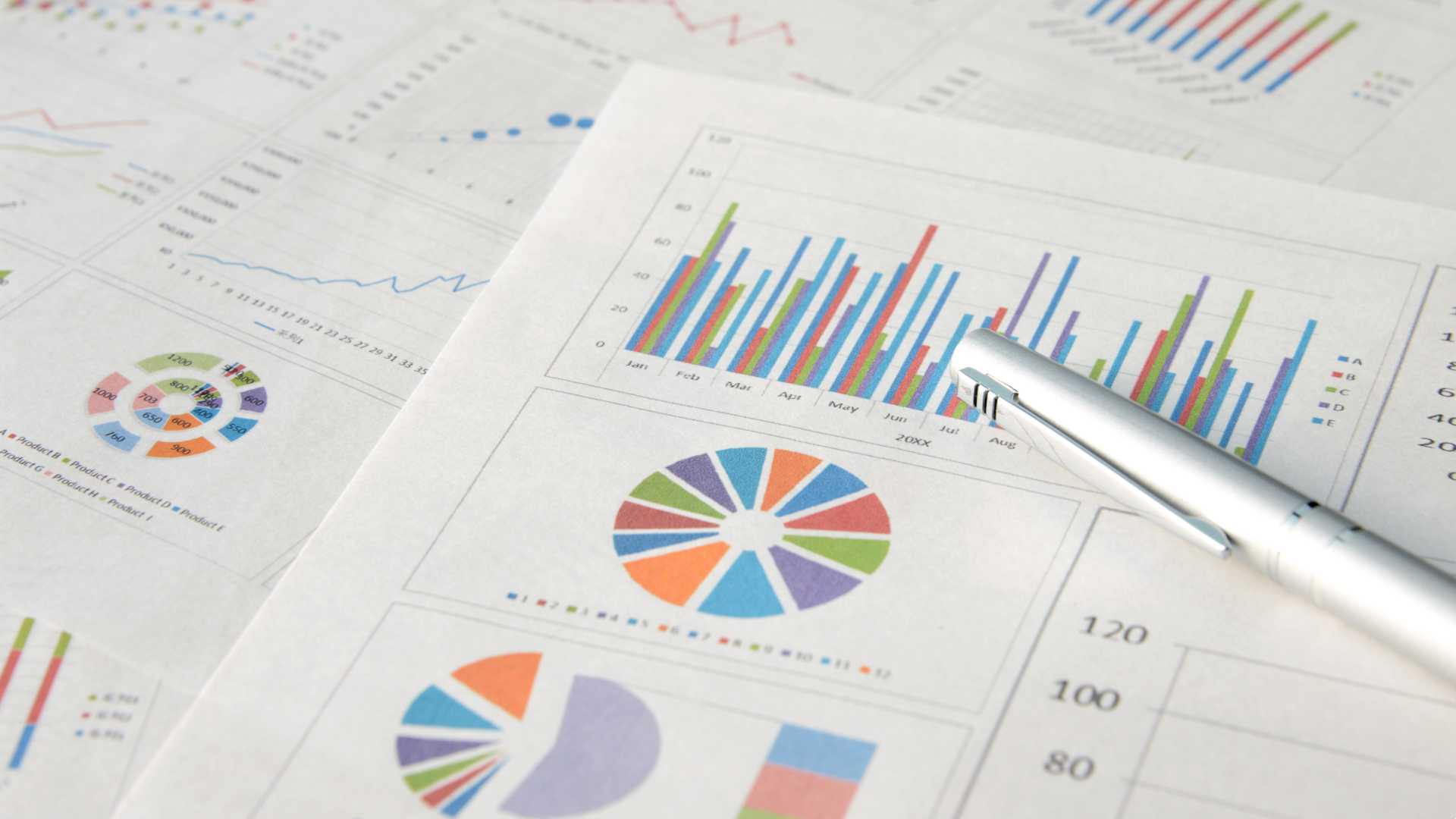 Measurement and analytics diagrams, charts and bar and line graphs on sheets of white paper and a white pen on top.