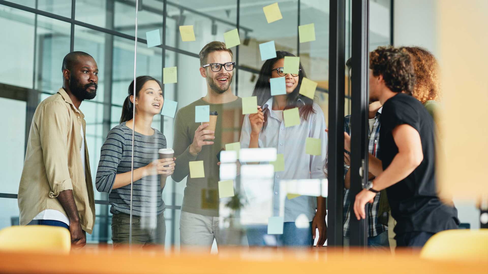 A team of coworkers collaborate while looking at sticky notes on a glass wall