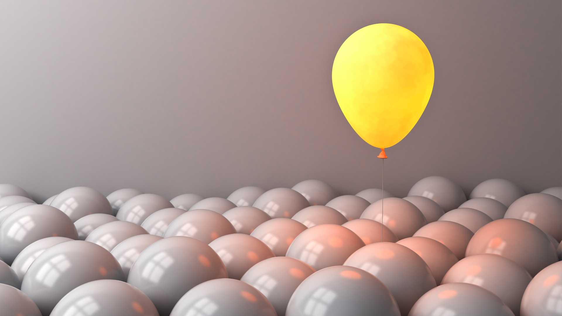 One yellow ballon floating above gray balloons against a gray background representing consciousness