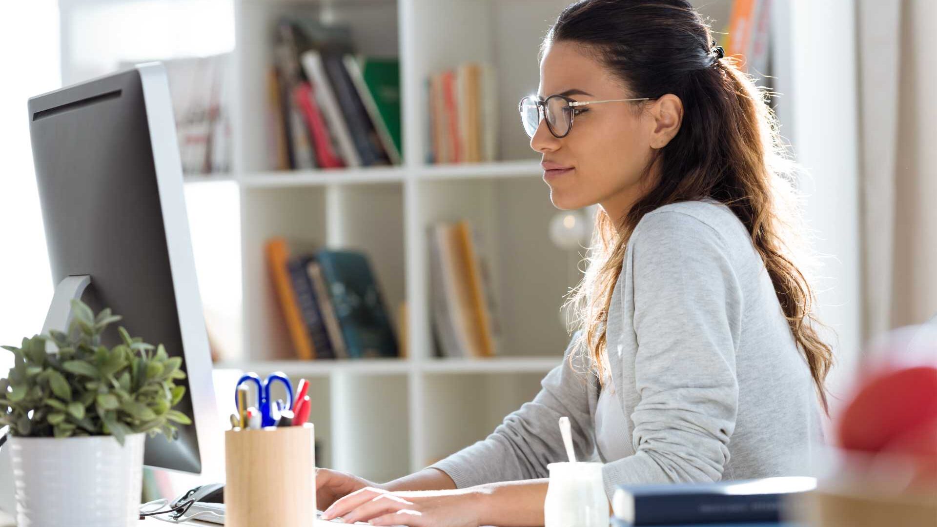 Businesswoman working remotely in front of a desktop with hands on keyboard