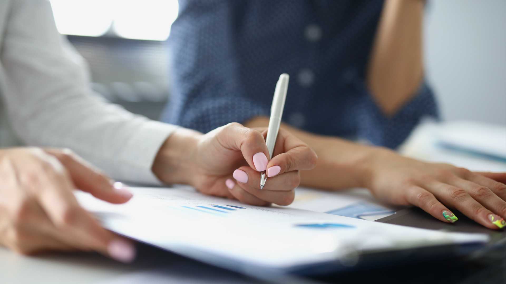 Businessperson writing on a clipboard on a sheet of paper with charts and graphs