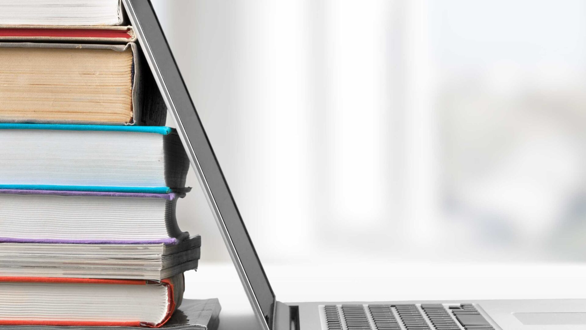 computer leaning on a colorful stack of books