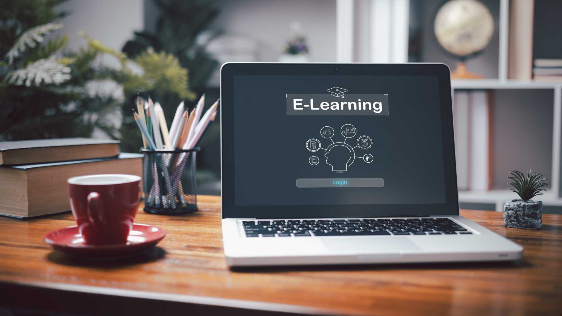 A laptop is open on a desk with "e-learning" on the screen along with related graphics