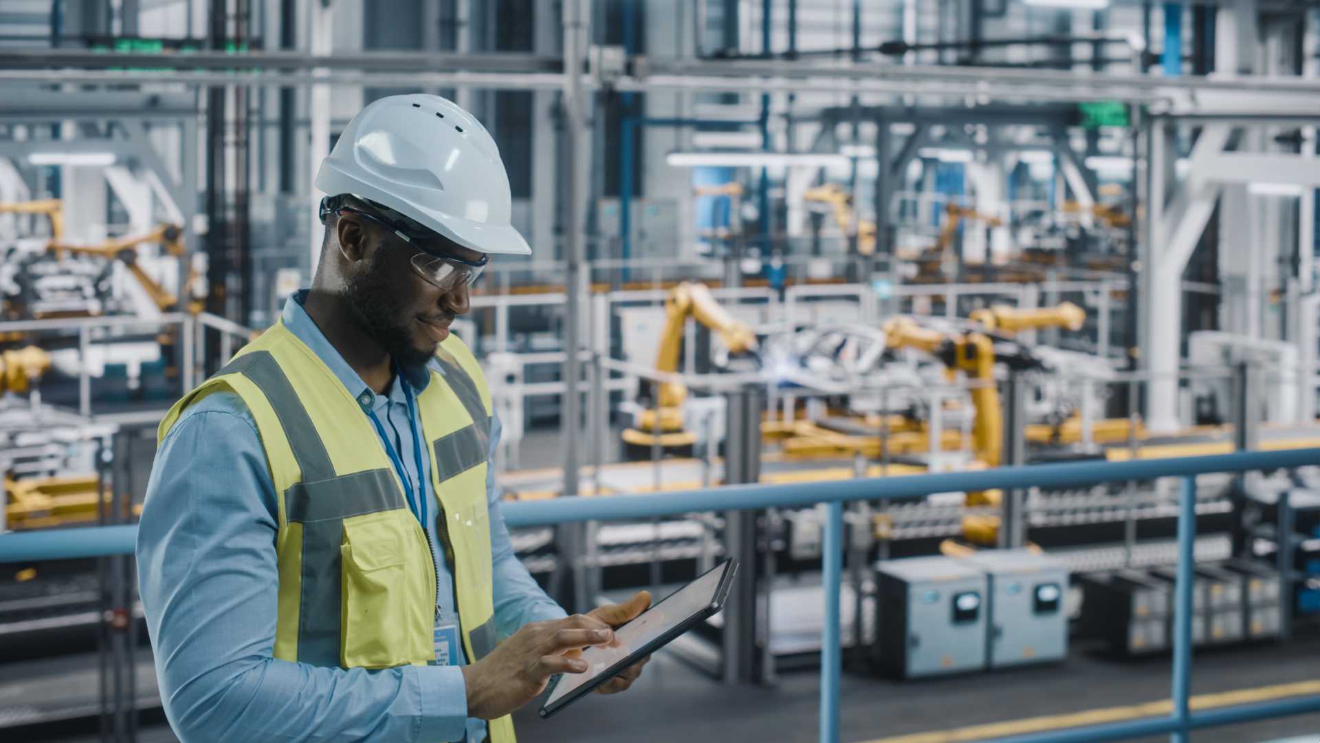Manufacturer worker wearing a white hardhat and safety goggles,, holding a digital work tablet that is powered by AI and automation to drive better performance and collect data for decision-making.