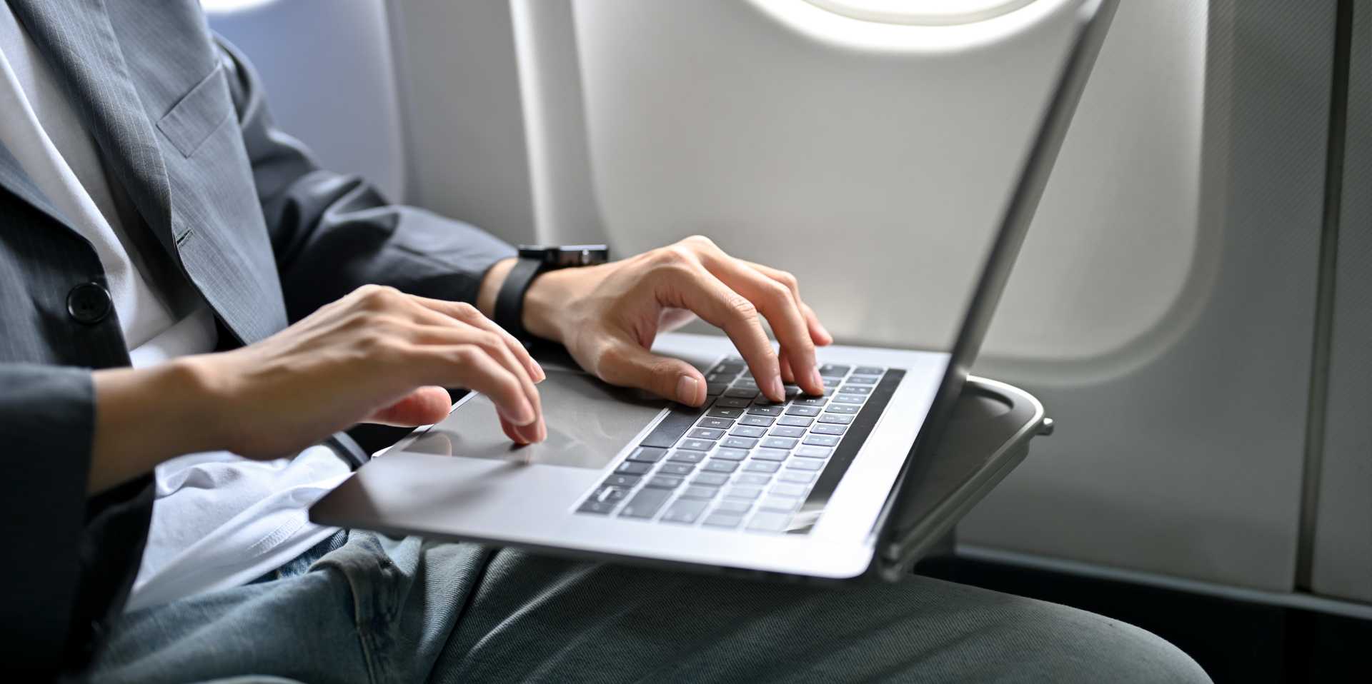 A businessman passenger using his laptop computer, working on his business task during travel on the plane.