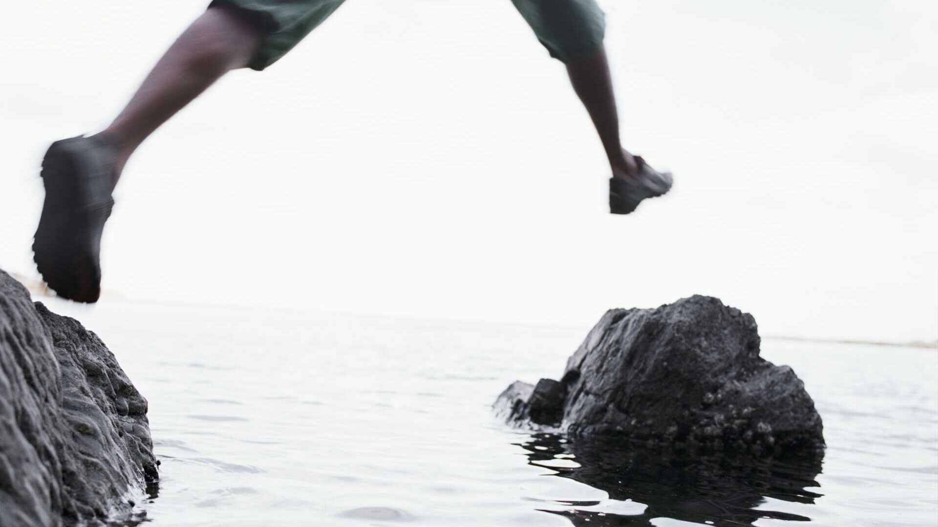 A person is in a body of water jumping from rock to rock
