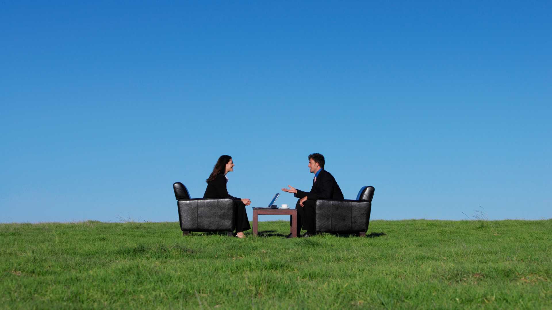 Two people sitting together outside on a grass hill discussing work.