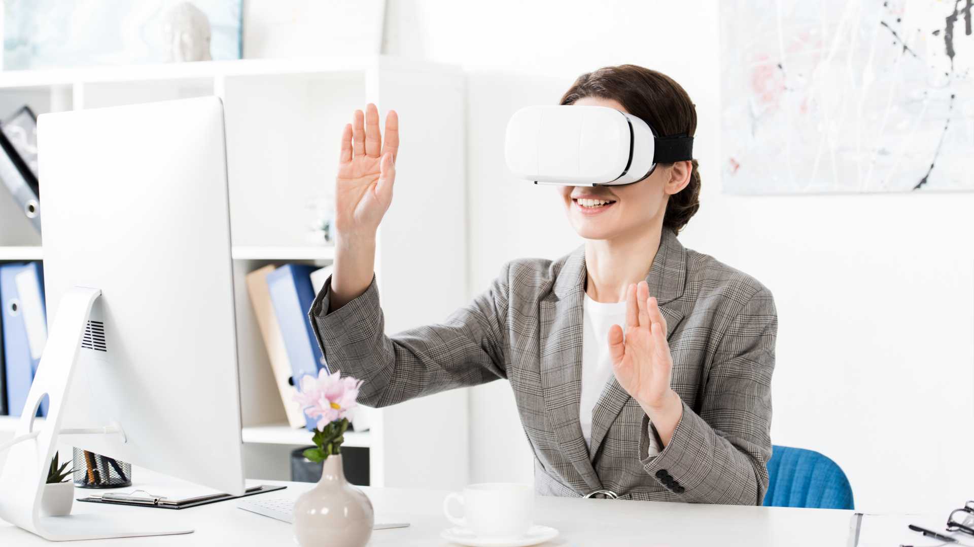 Businesswoman wearing a virtual reality (VR) headset in front of a desktop computer.