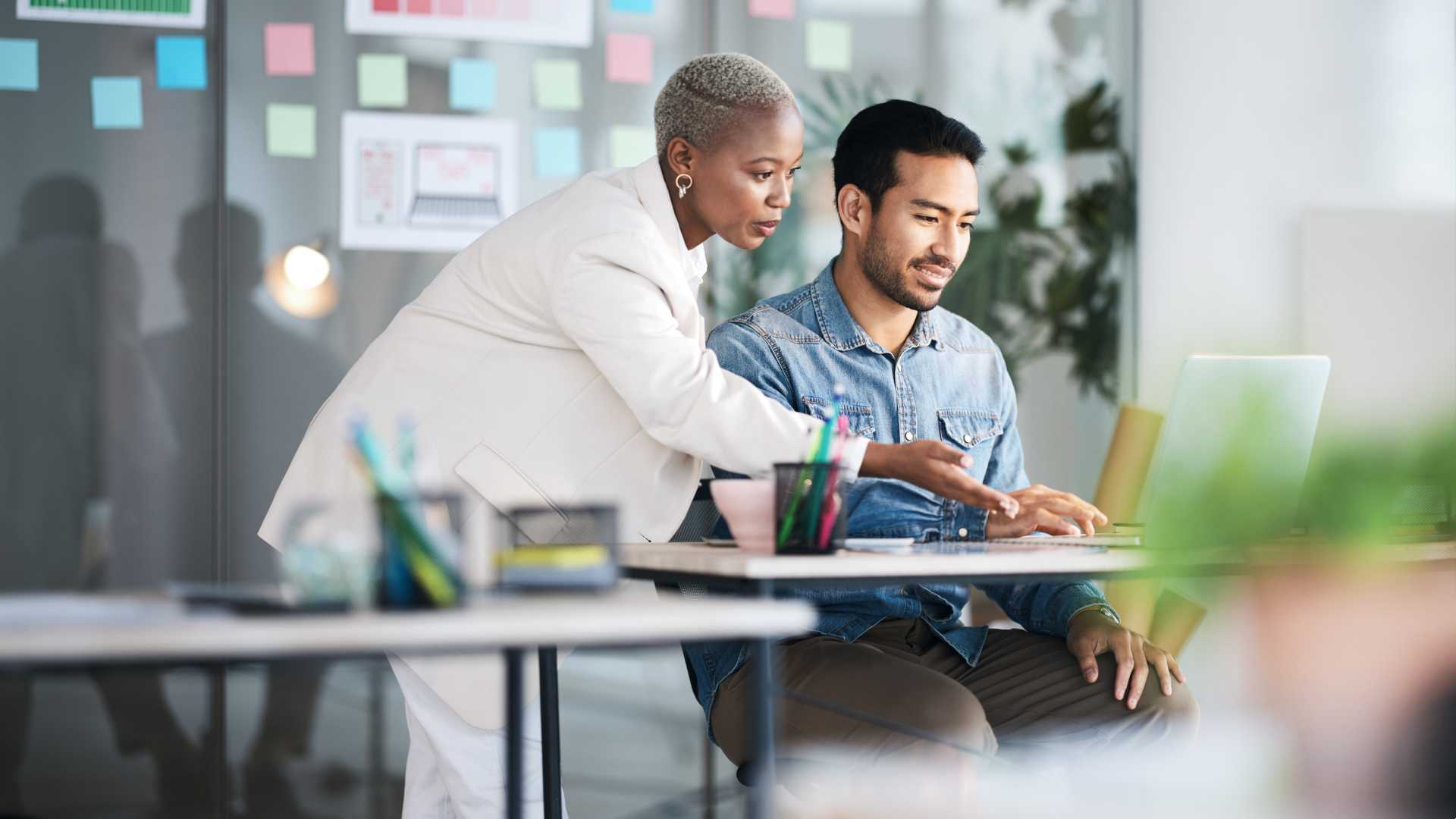 Woman teaching her Co-worker how to do something on the laptop.