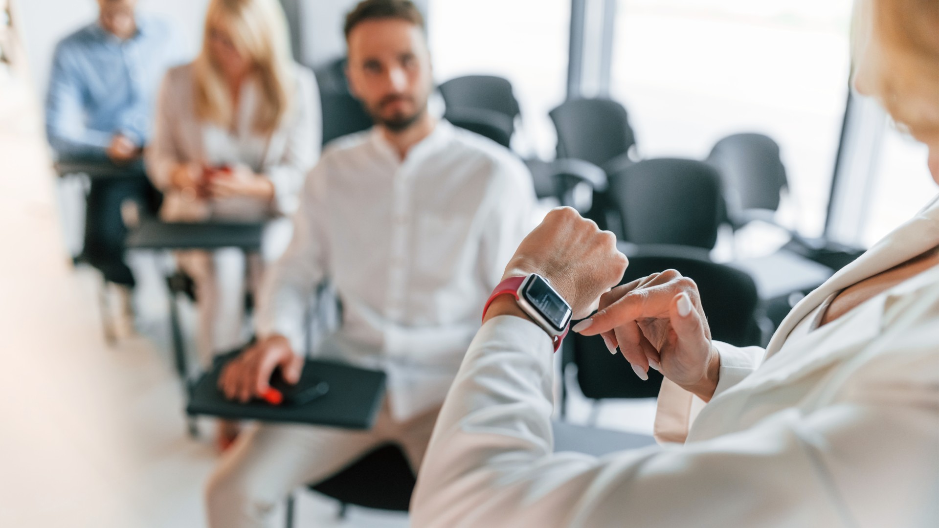 Classroom in the background with an instructor looking at their watch in the foreground