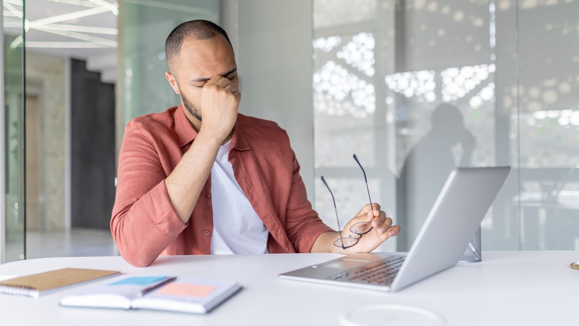 Man sitting at a desk with a laptop and holding his head, illustrating burnout and change fatigue in the workplace