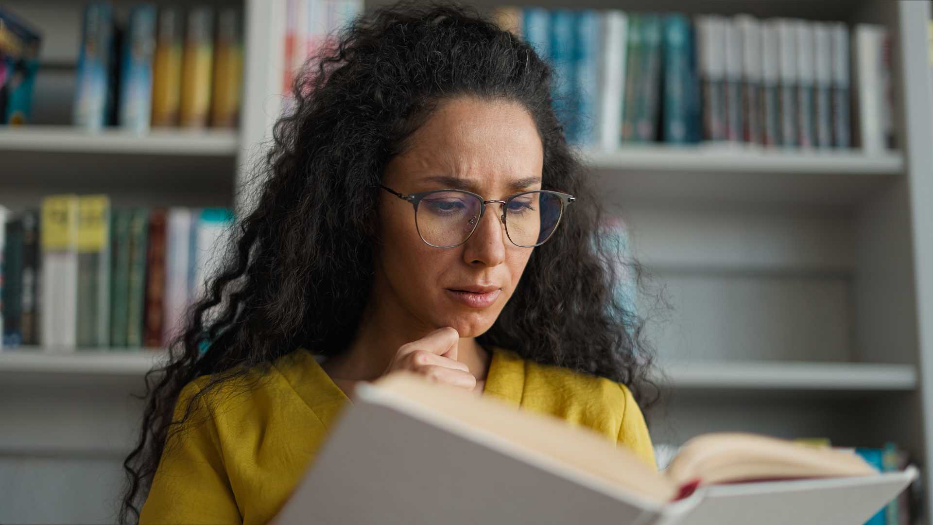 a woman with glasses looks inquisitively at an open book