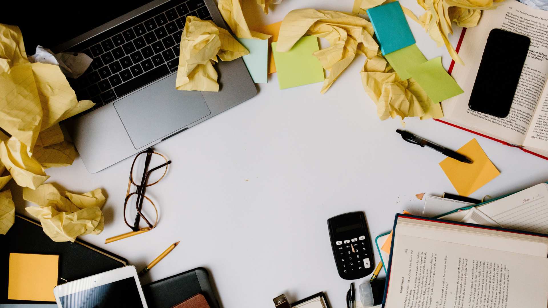 A cluttered desk with scattered papers, pens, and other tools.