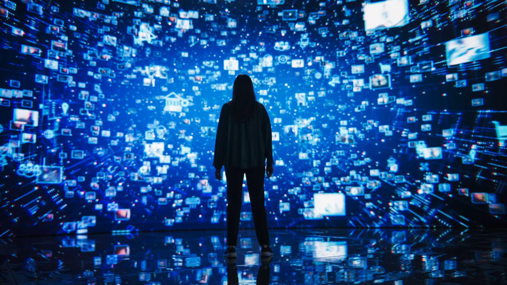 person standing before a large immersive digital display filled with interconnected images, data and media, representing AI-powered learning, information networks and emerging technologies