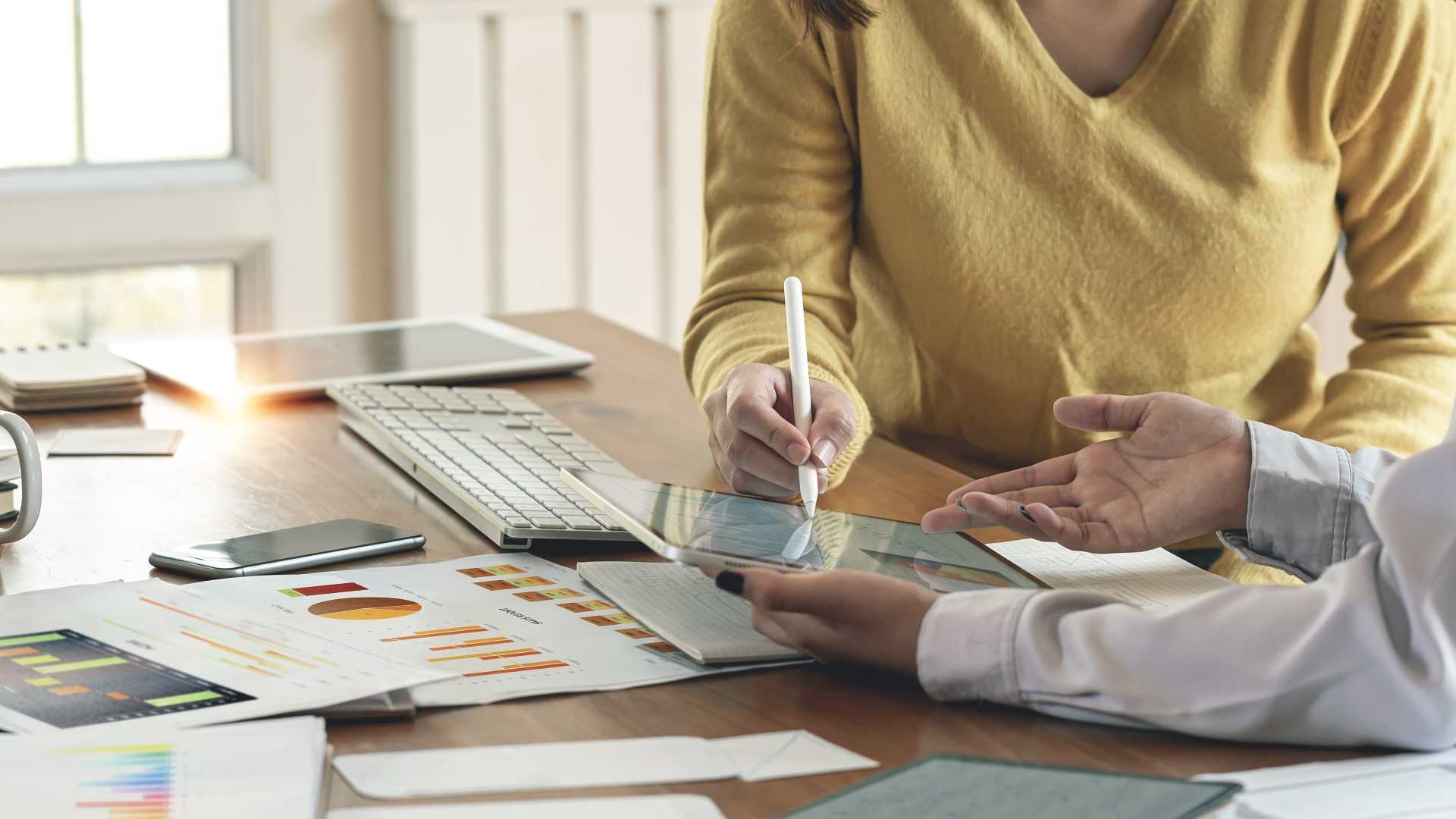 Learning and development professionals review workload and project planning data on a tablet and printed reports, illustrating capacity planning, resource allocation and data-driven training decisions.