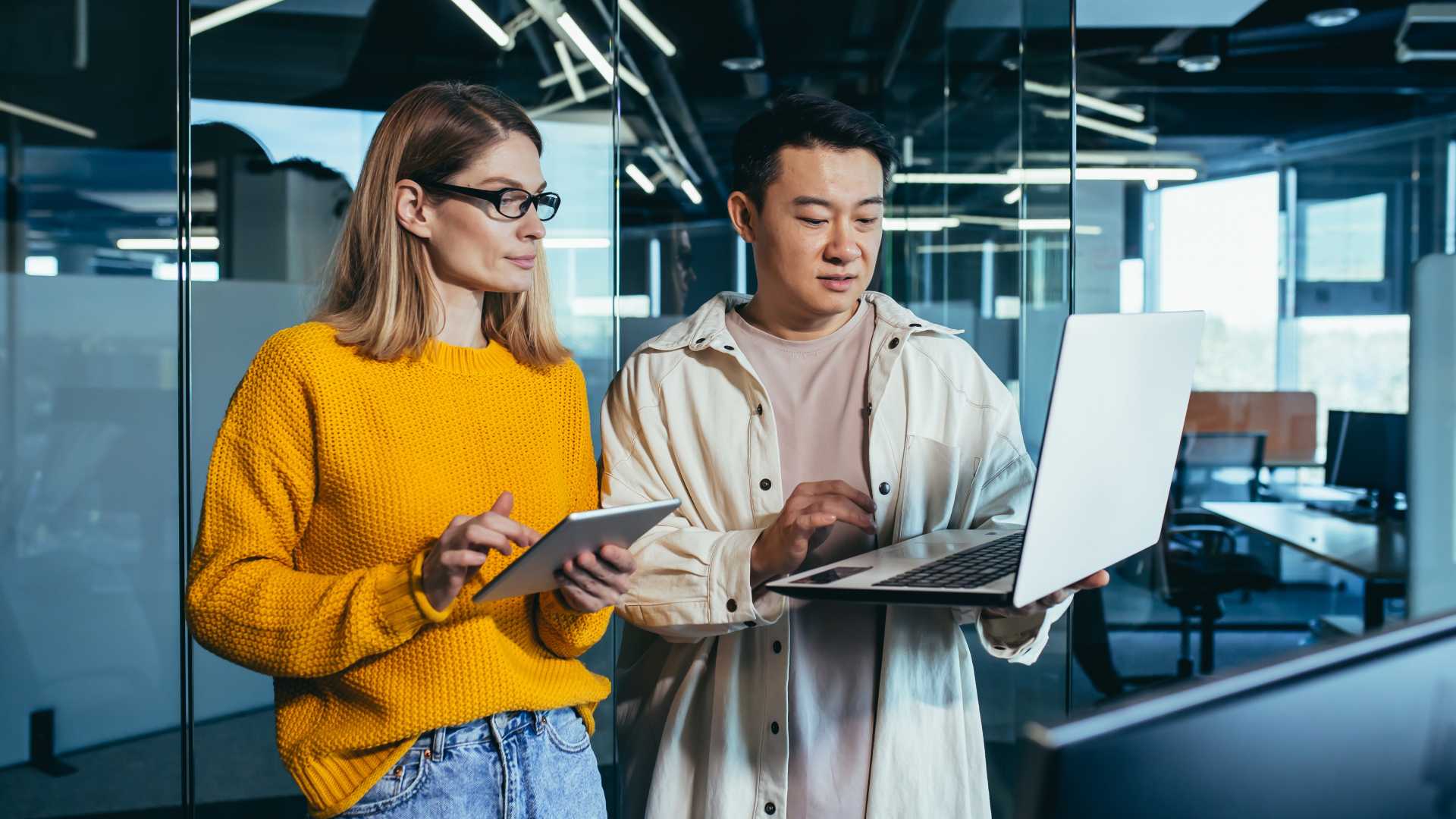 Two employees collaborate on an AI-enabled workflow, reviewing information on a laptop and tablet to test and refine a practical workplace solution during hands-on AI training.