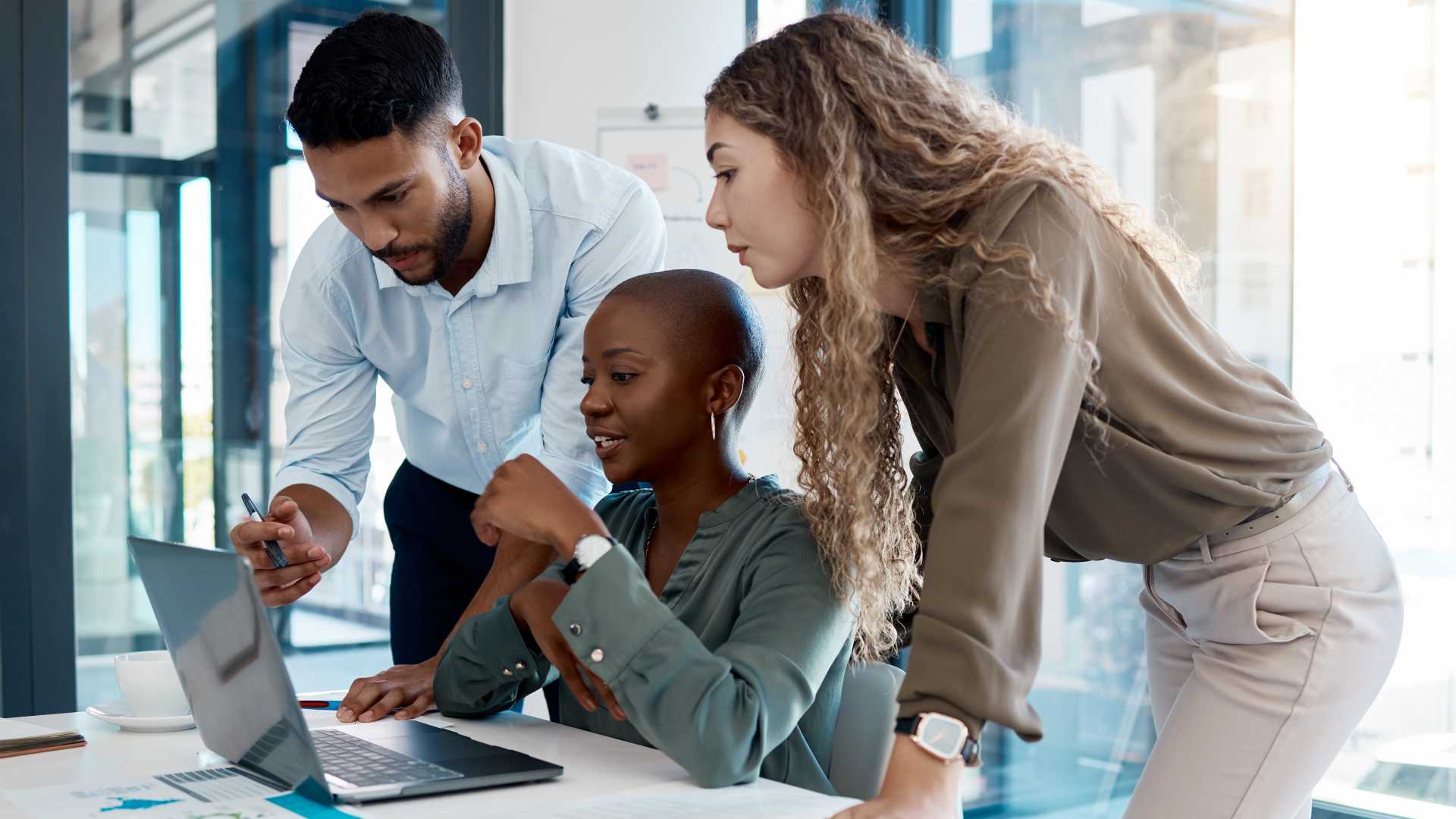 Three colleagues collaborate around a laptop, illustrating coaching, peer learning and structured learning pathways that support early-career development in an AI-enabled workplace.