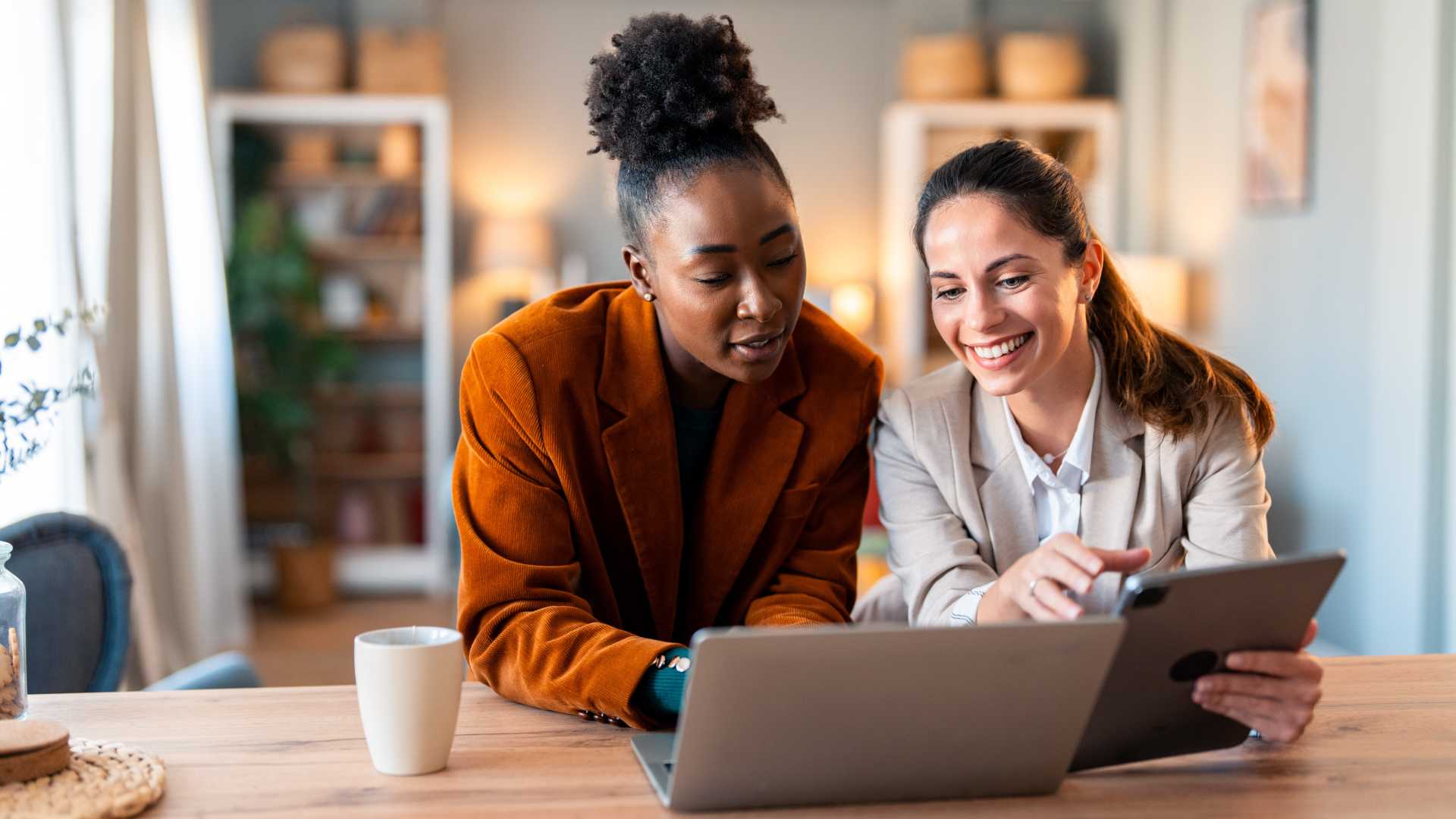 Two colleagues review information together on a tablet and laptop during a coaching session, illustrating constructive feedback, collaboration and leadership development.