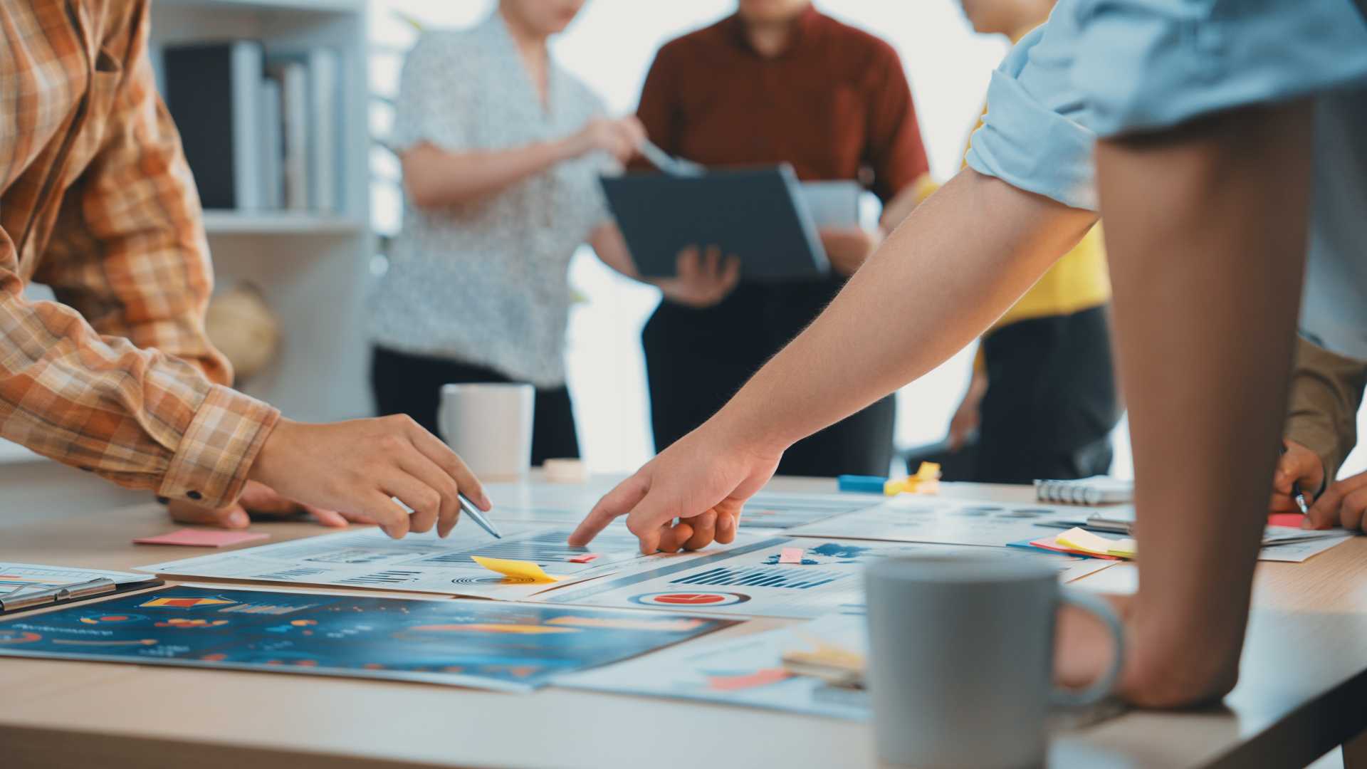 Team members collaborate around a table, reviewing charts, dashboards and printed reports while discussing business performance and measurement metrics during a planning meeting.