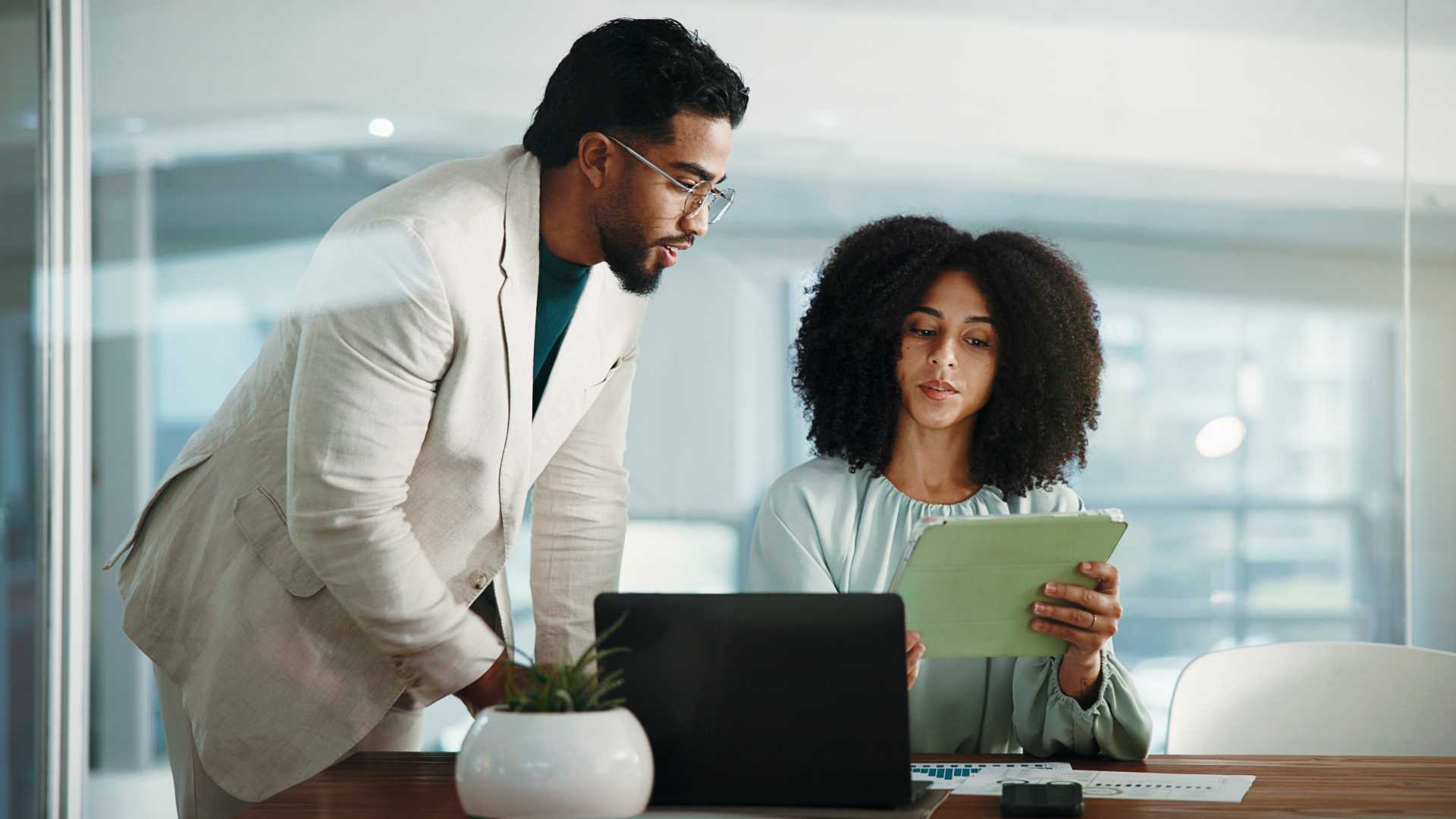 Manager and new employee review work together on a tablet and laptop, illustrating hands-on coaching and on-the-job learning during onboarding.