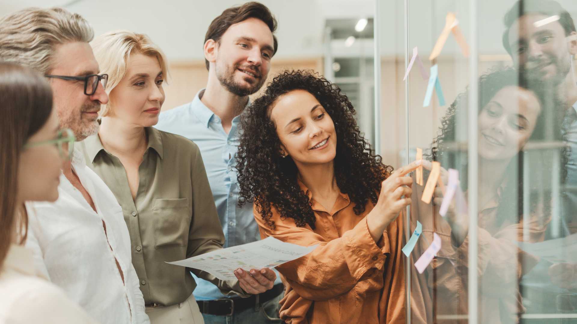 L&D professionals collaborate around a glass wall with sticky notes, representing teamwork, structured processes and organizational planning.